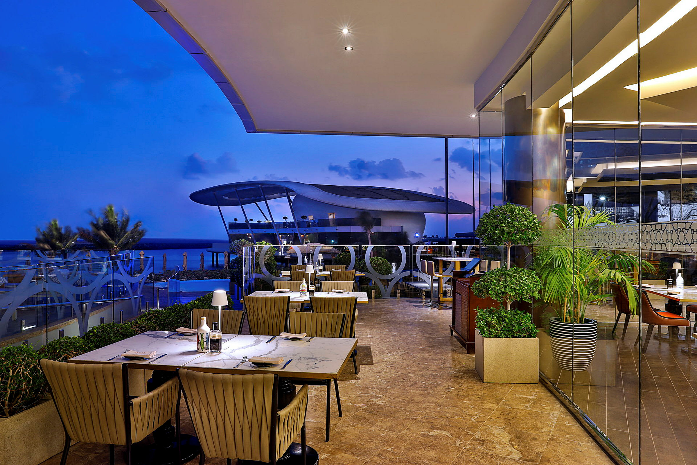 En restaurang med utsikt över havet och en futuristisk byggnad i bakgrunden. (AI-genererad text)