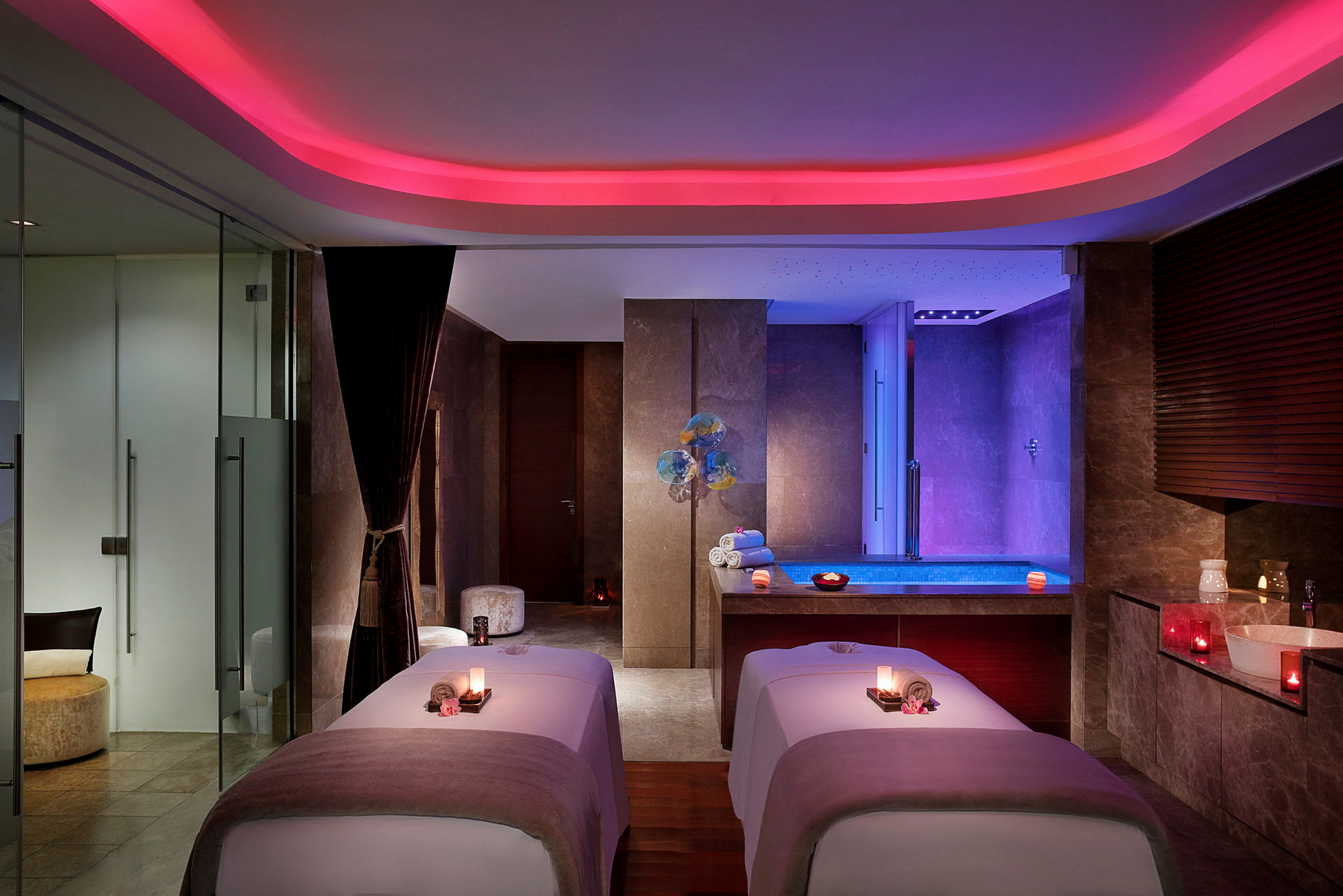 Ett elegant spa-rum med två massagebänkar och ett upplyst poolområde i bakgrunden. (AI-genererad text)