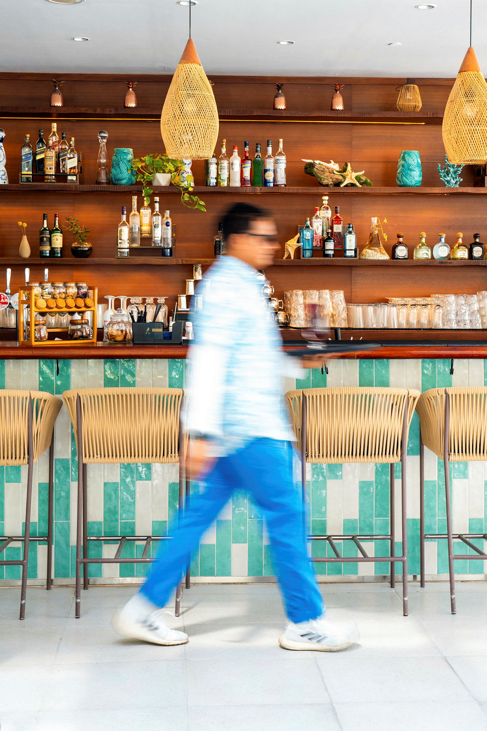 En bar med trädetaljer och hyllor fyllda med flaskor och glas. En person går förbi i förgrunden. (AI-genererad text)
