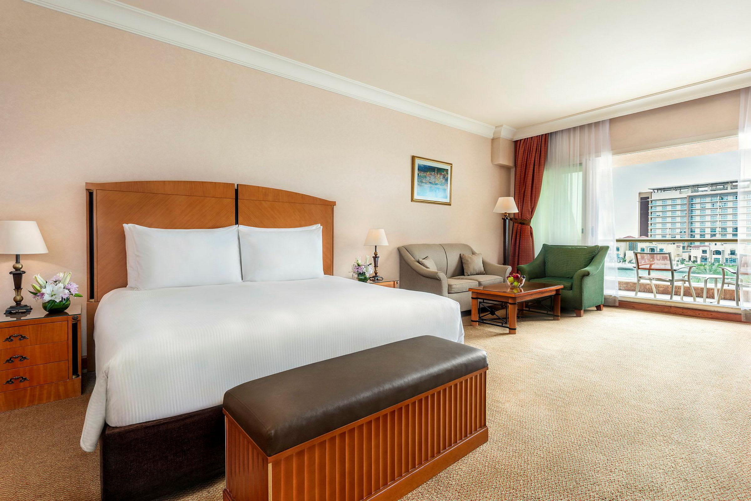 Hotellrum med en dubbelsäng, soffgrupp och utsikt över en byggnad genom fönstret. (AI-genererad text)