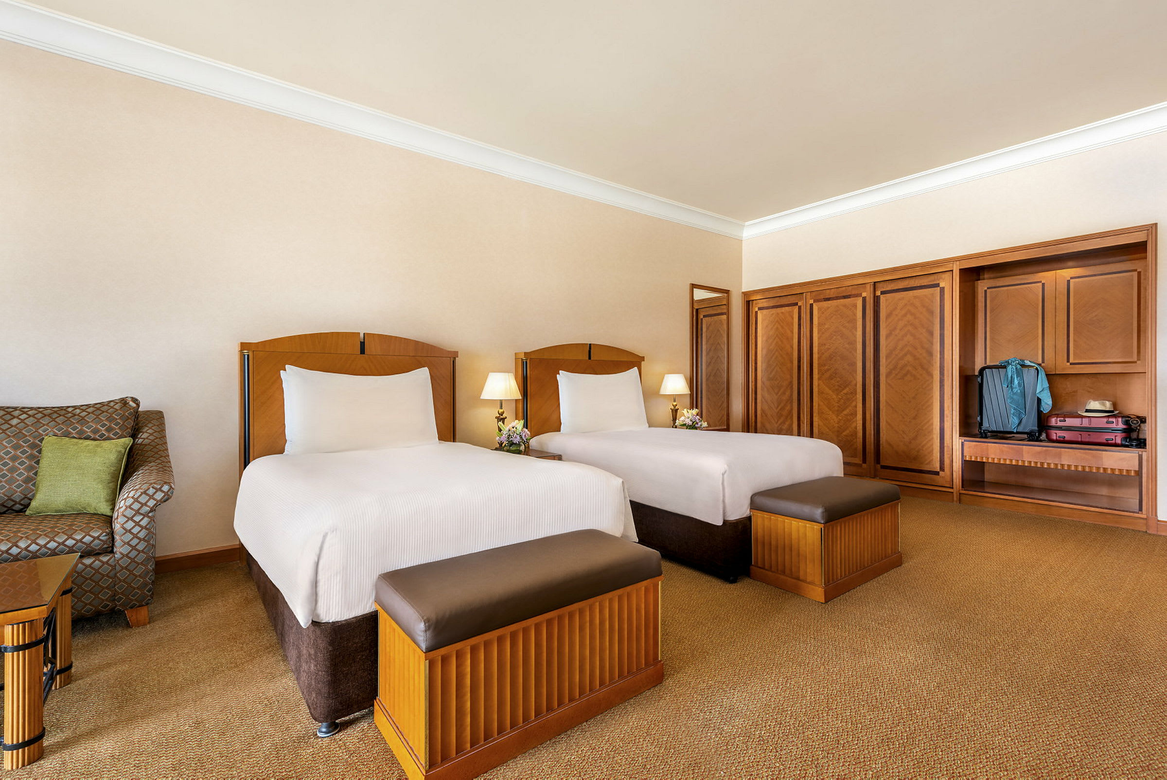 Två enkelsängar i ett hotellrum med en sittande fåtölj och garderober. (AI-genererad text)