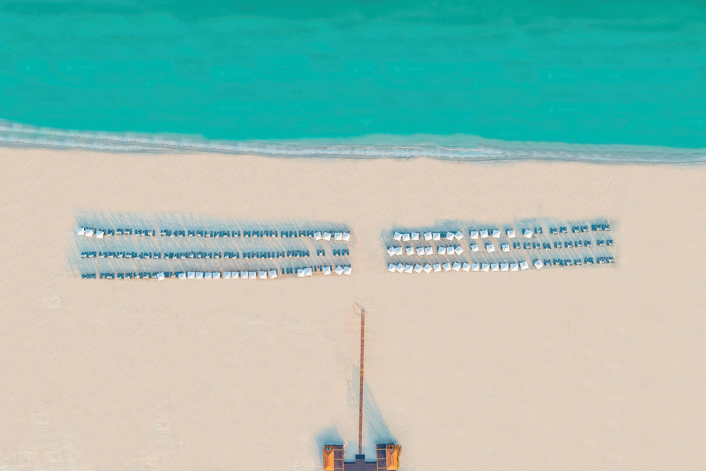 Flygfoto av en strand med solstolar och parasoller vid havet. (AI-genererad text)