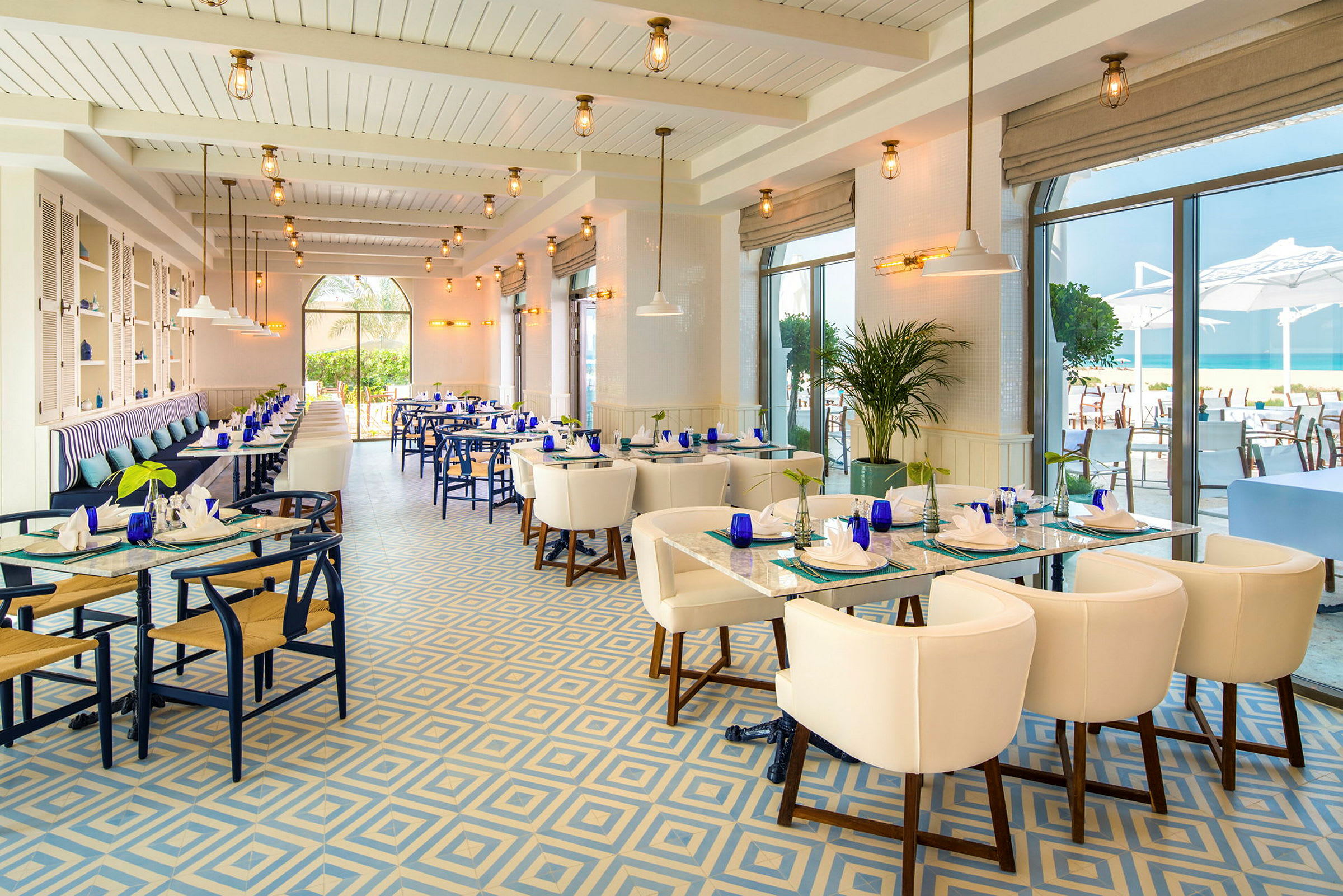 En elegant restaurang med stora fönster, blå och vita färgscheman och utsikt mot havet. (AI-genererad text)