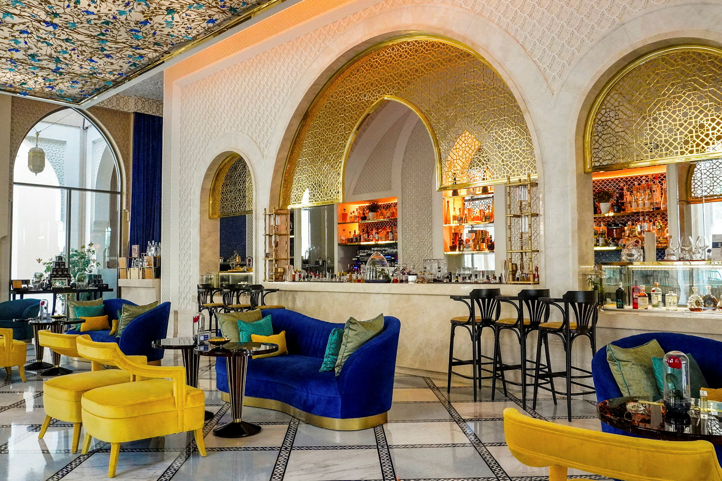 En elegant lounge med blå och gula möbler, ett dekorativt tak och en bar med gyllene accenter. (AI-genererad text)