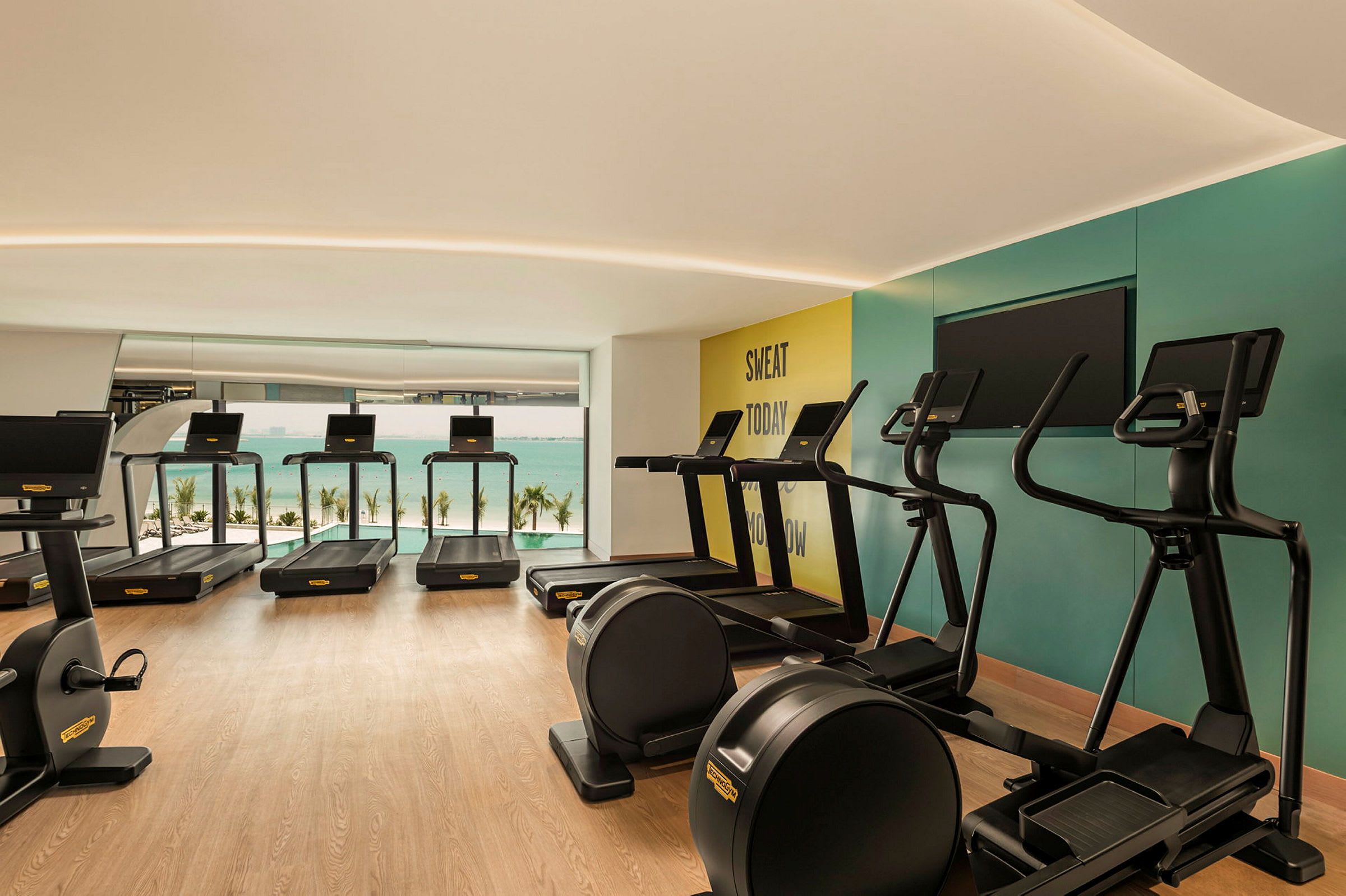 Ett modernt gym med löpband, träningscyklar och en utsikt mot havet. (AI-genererad text)