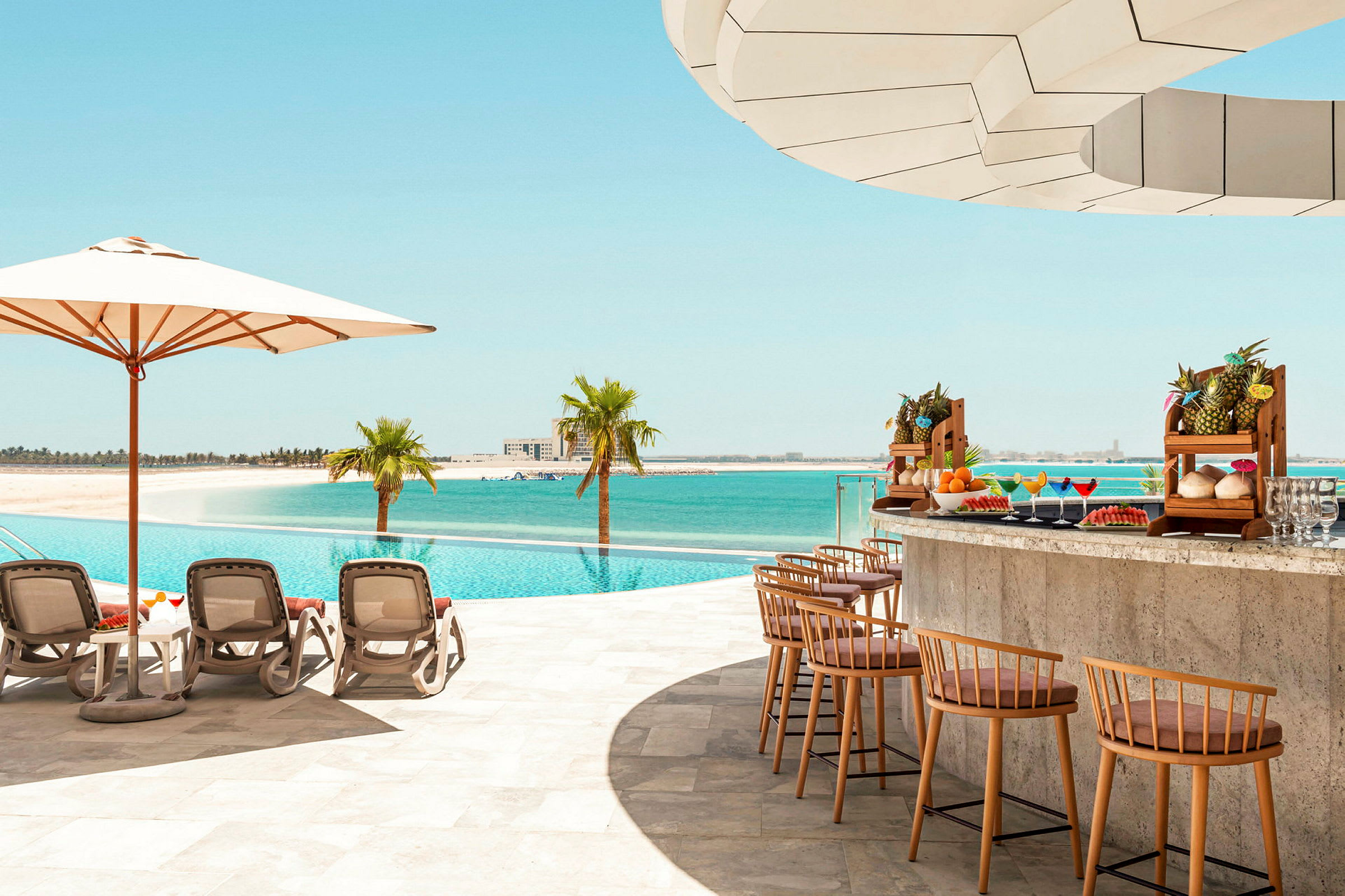 En pool vid stranden med solstolar, parasoll och en poolbar med exotiska frukter. (AI-genererad text)
