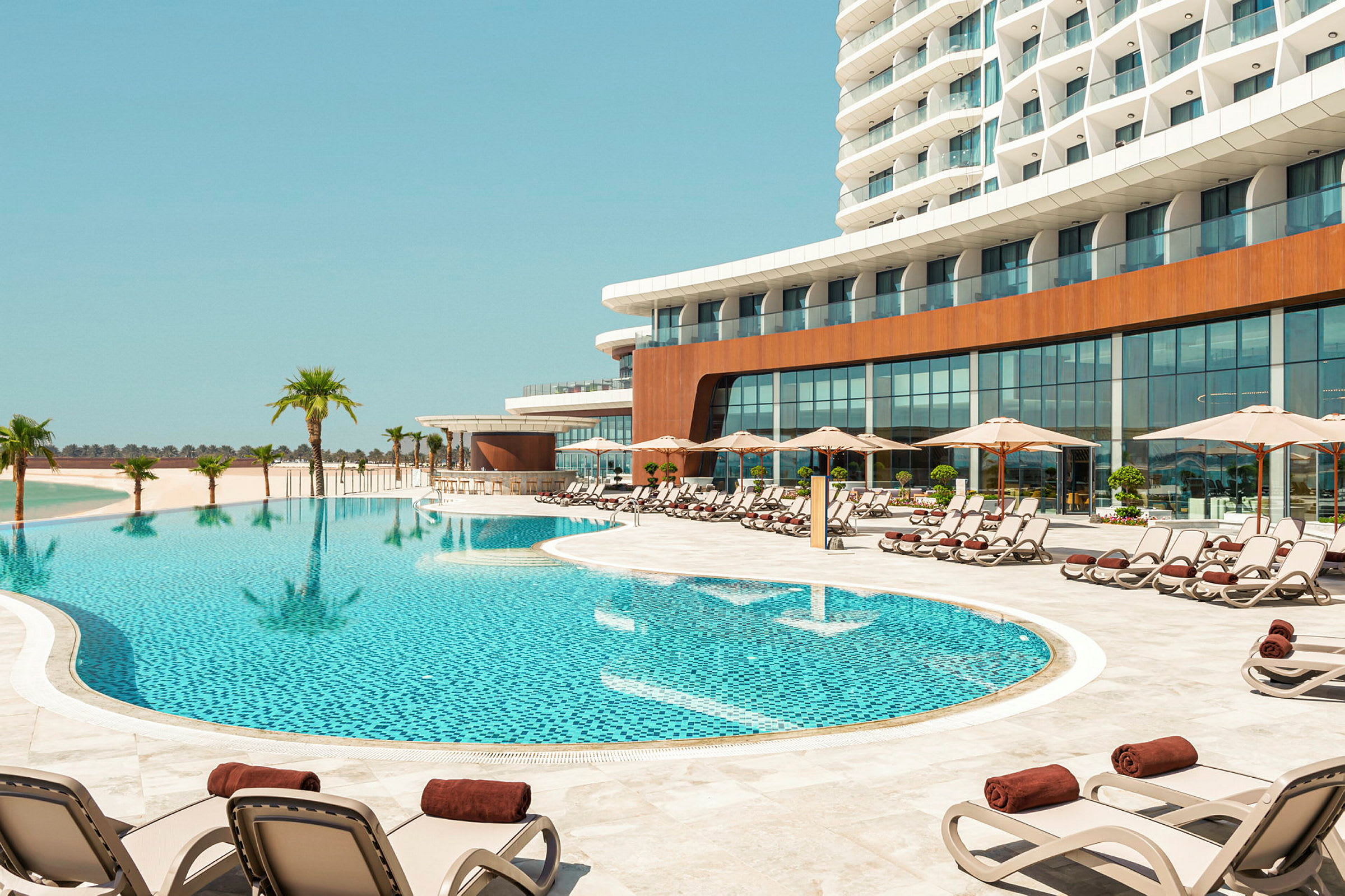 En utomhuspool omgiven av solstolar under parasoller vid en modern hotellbyggnad. (AI-genererad text)