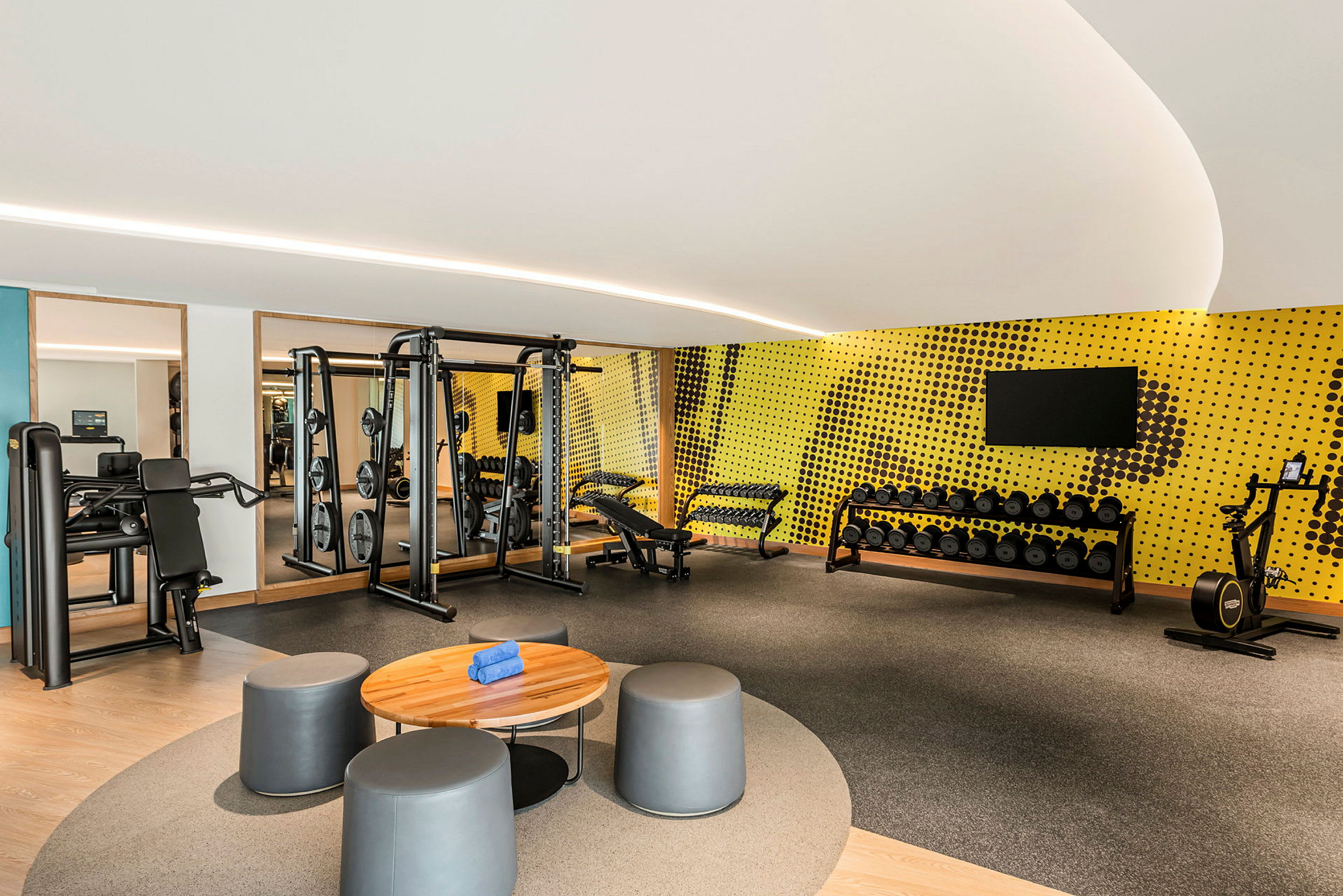 Ett modernt gym med träningsutrustning inklusive maskiner, vikter och en motionscykel i ett rum med gul väggdekoration. (AI-genererad text)