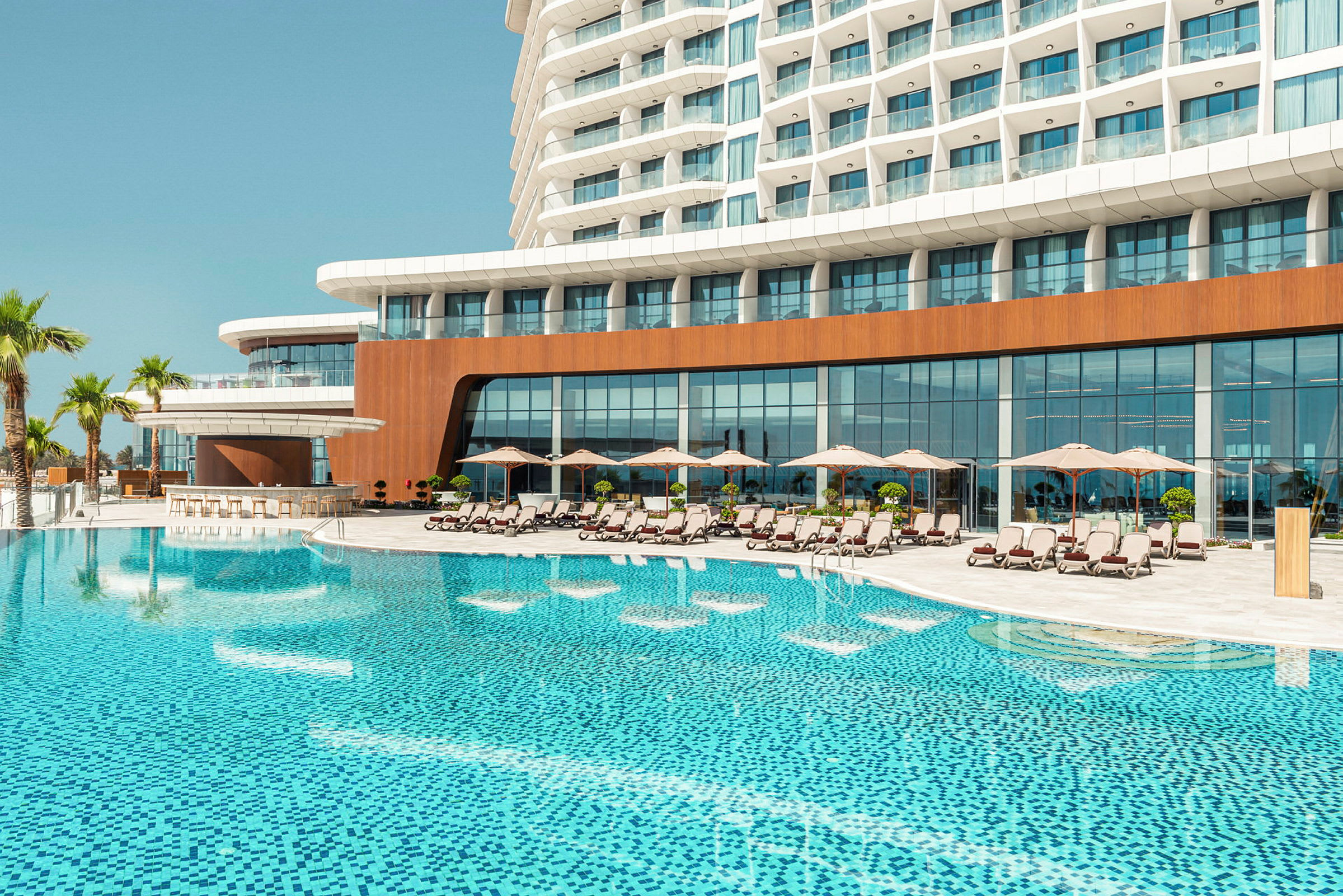 Ett hotellkomplex med en stor pool framför, omgivet av solstolar och parasoller. (AI-genererad text)