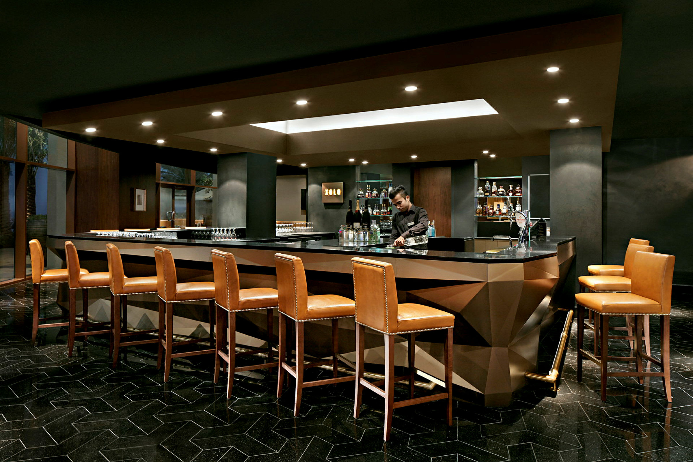 En elegant bar med höga läderstolar placerade runt en modern bardisk, i en väldesignad interiör. (AI-genererad text)