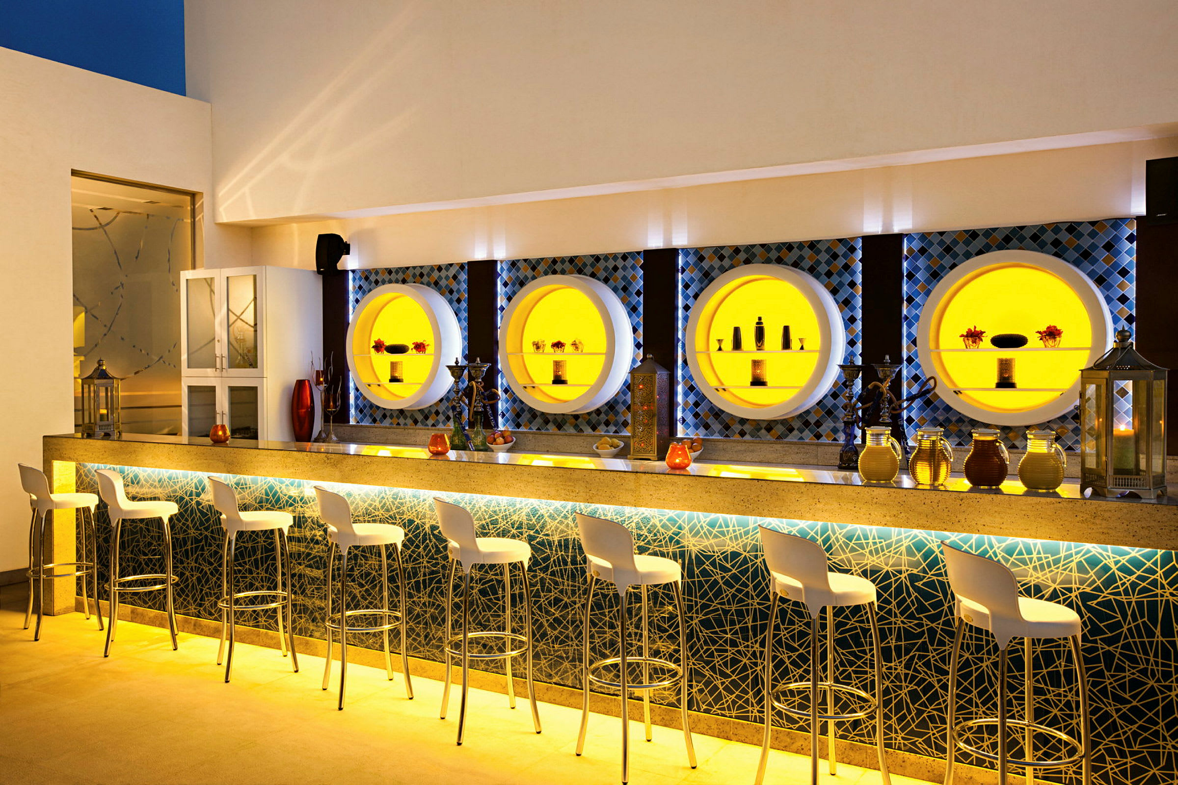 En upplyst bar med höga stolar och dekorativa hyllor på väggen. (AI-genererad text)