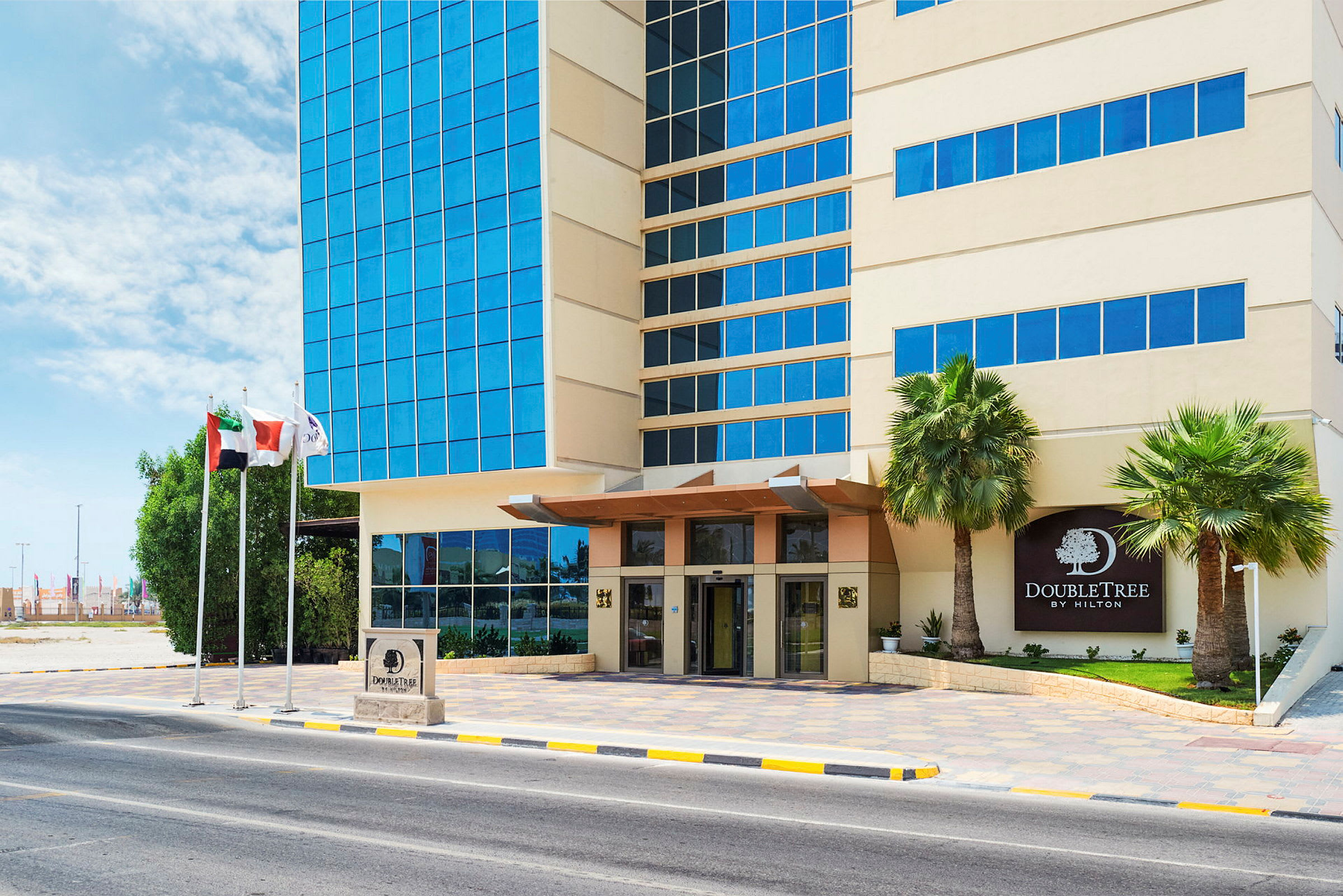 Exteriör av DoubleTree Hotel med ingång, glasfasad och palmer vid sidan. (AI-genererad text)