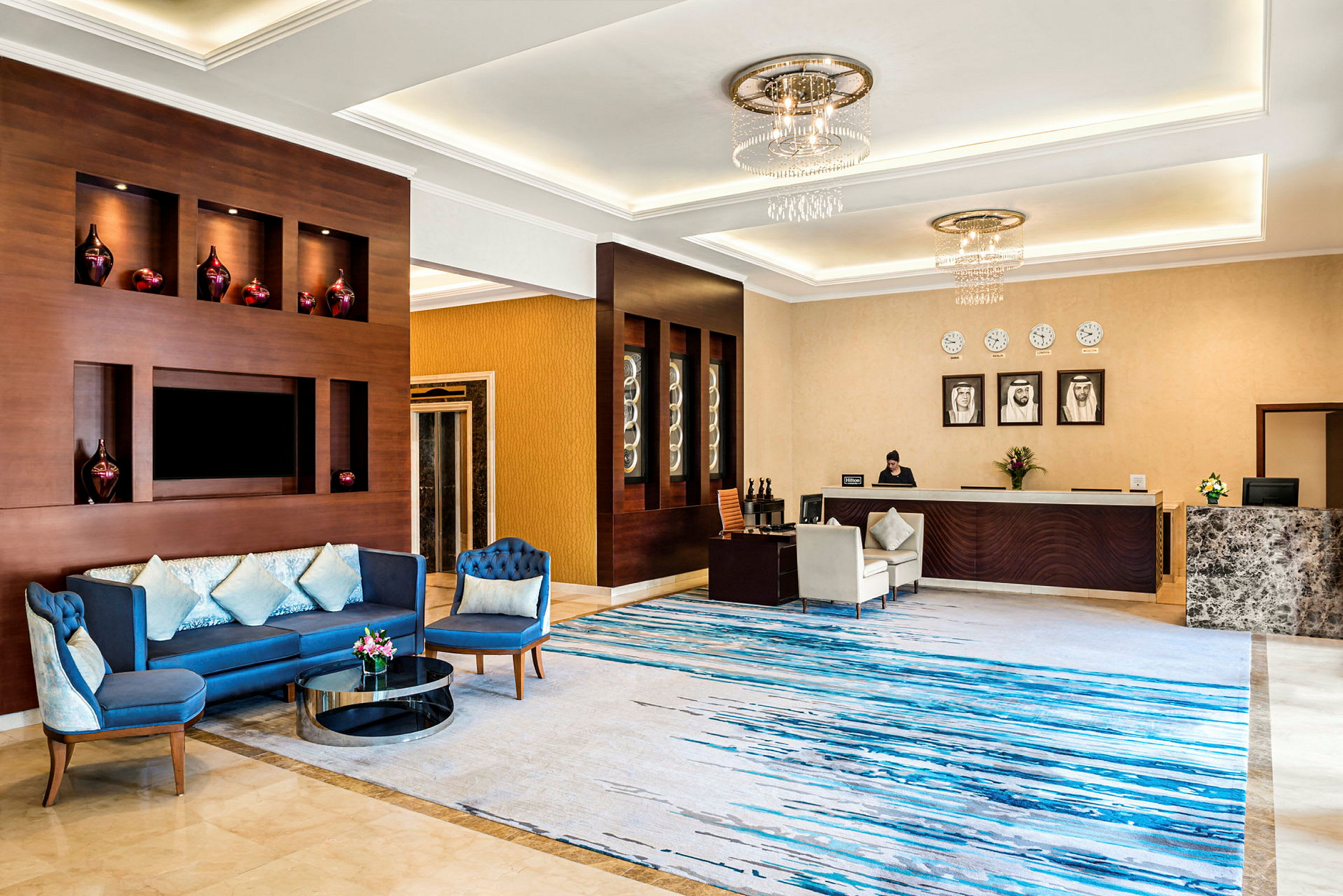 Ett elegant hotellobby med en sittgrupp med blå soffor, ett dekorativt framträdande receptionsområde och ett marmorgolv. (AI-genererad text)