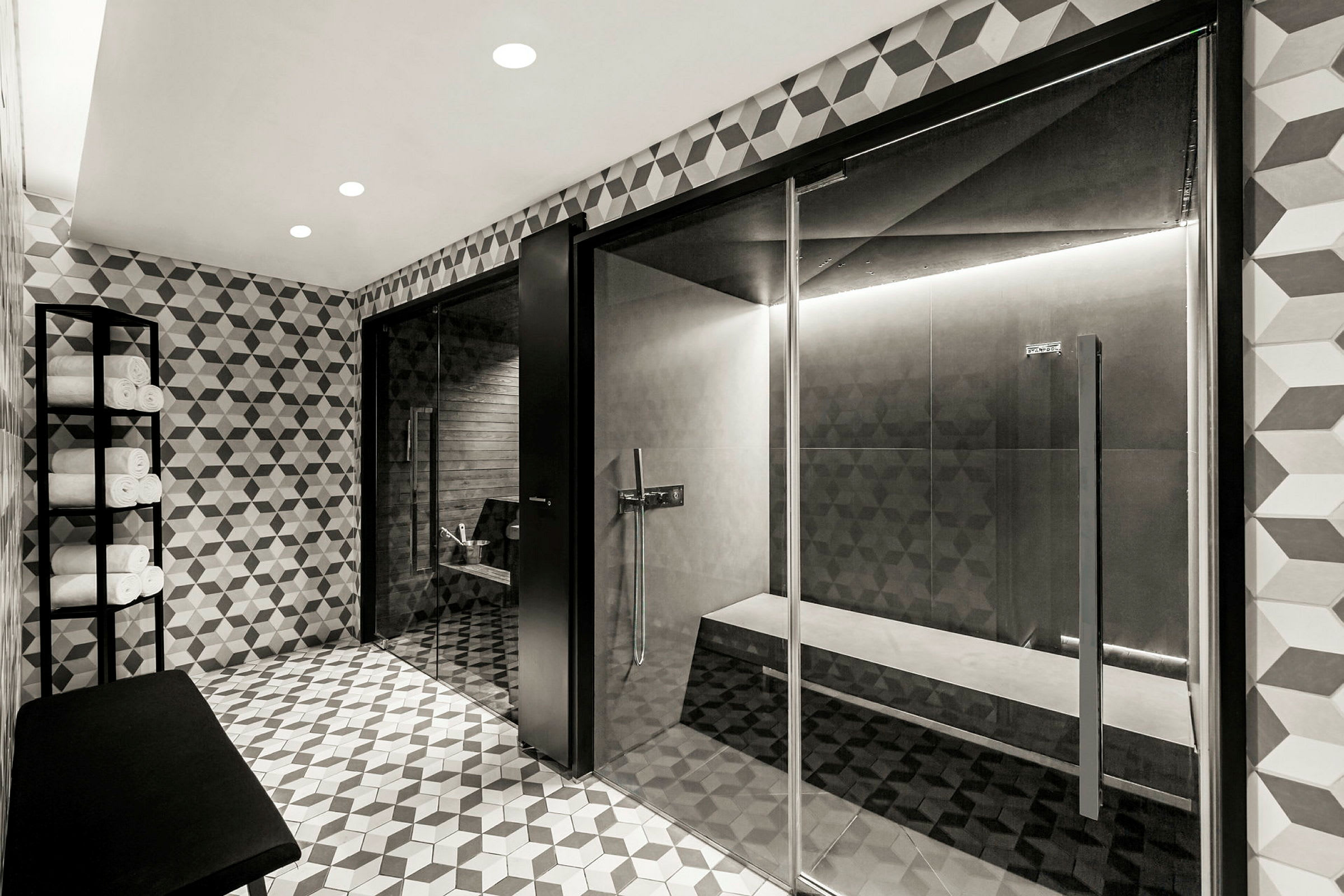 Ett modernt spa med kaklad inredning, sittbänkar och handdukar som är upplagda på en metallhylla. (AI-genererad text)