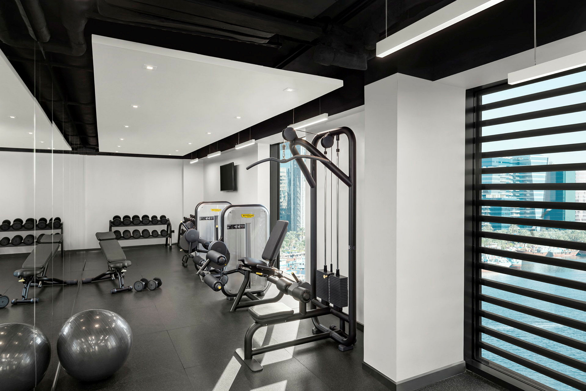 Ett gym med träningsutrustning, vikter och en bänk, med fönster som visar en utomhusutsikt. (AI-genererad text)