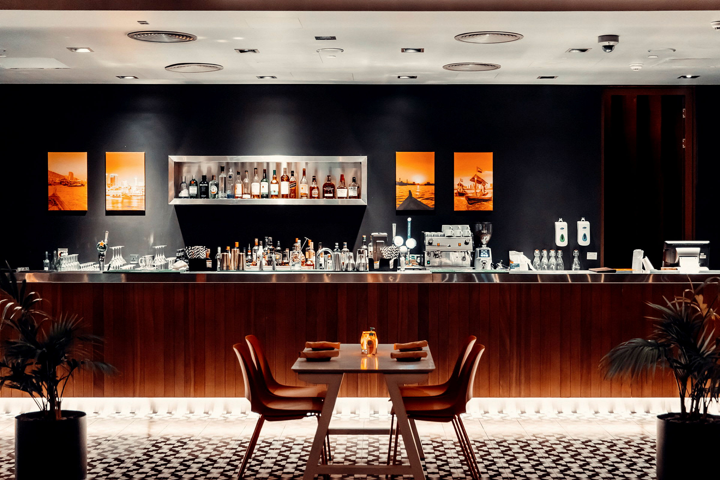 En elegant bar med hyllor fyllda med flaskor, en bänk med bartillbehör och ett dukat bord för gästerna i förgrunden. (AI-genererad text)