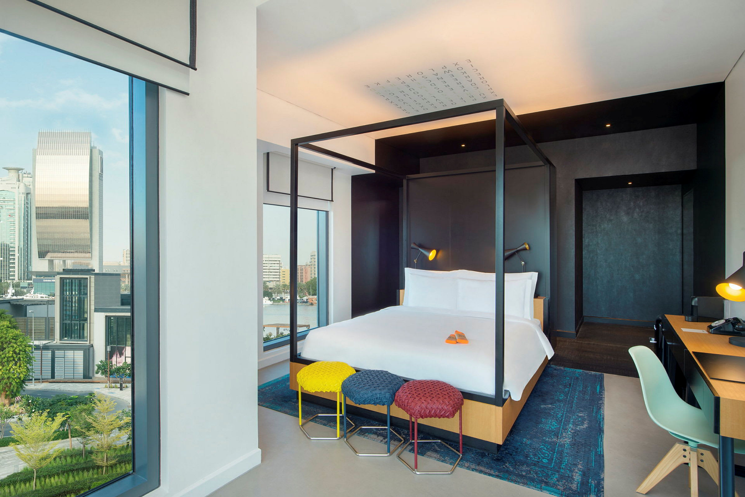 Modernt hotellrum med en himmelssäng, skrivbord och stora fönster med utsikt över staden. (AI-genererad text)