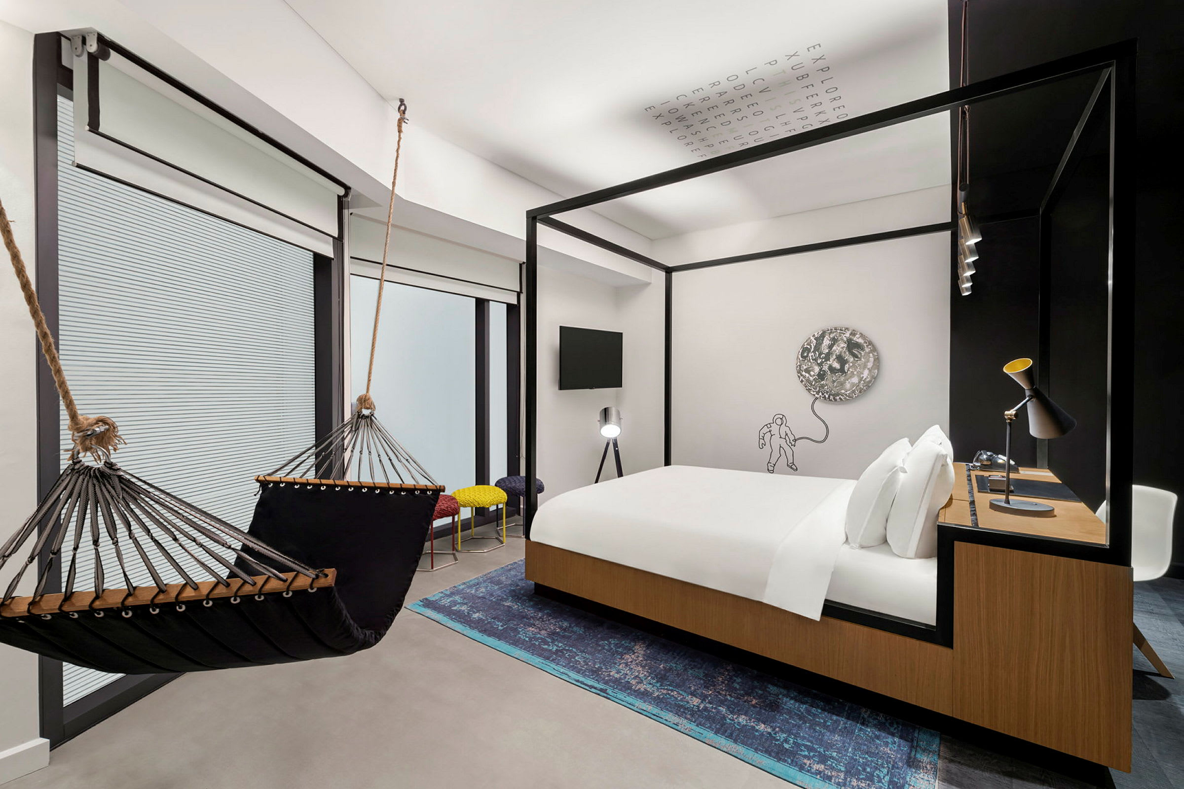 Ett modernt hotellrum med en hängmatta, en dubbelsäng med trädetaljer, ett skrivbord och en konstnärlig väggdekoration. (AI-genererad text)
