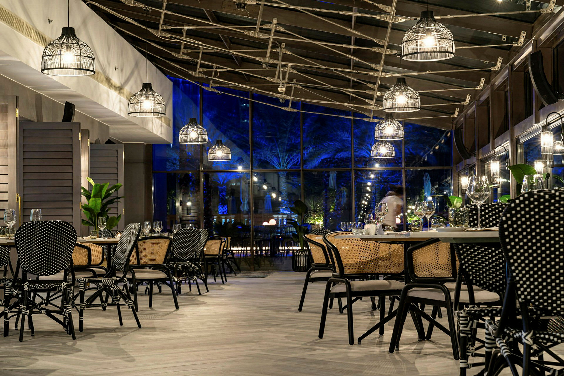 En restaurang med moderna möbler och taklampor, samt glasväggar som visar kvällsbelysning utomhus. (AI-genererad text)
