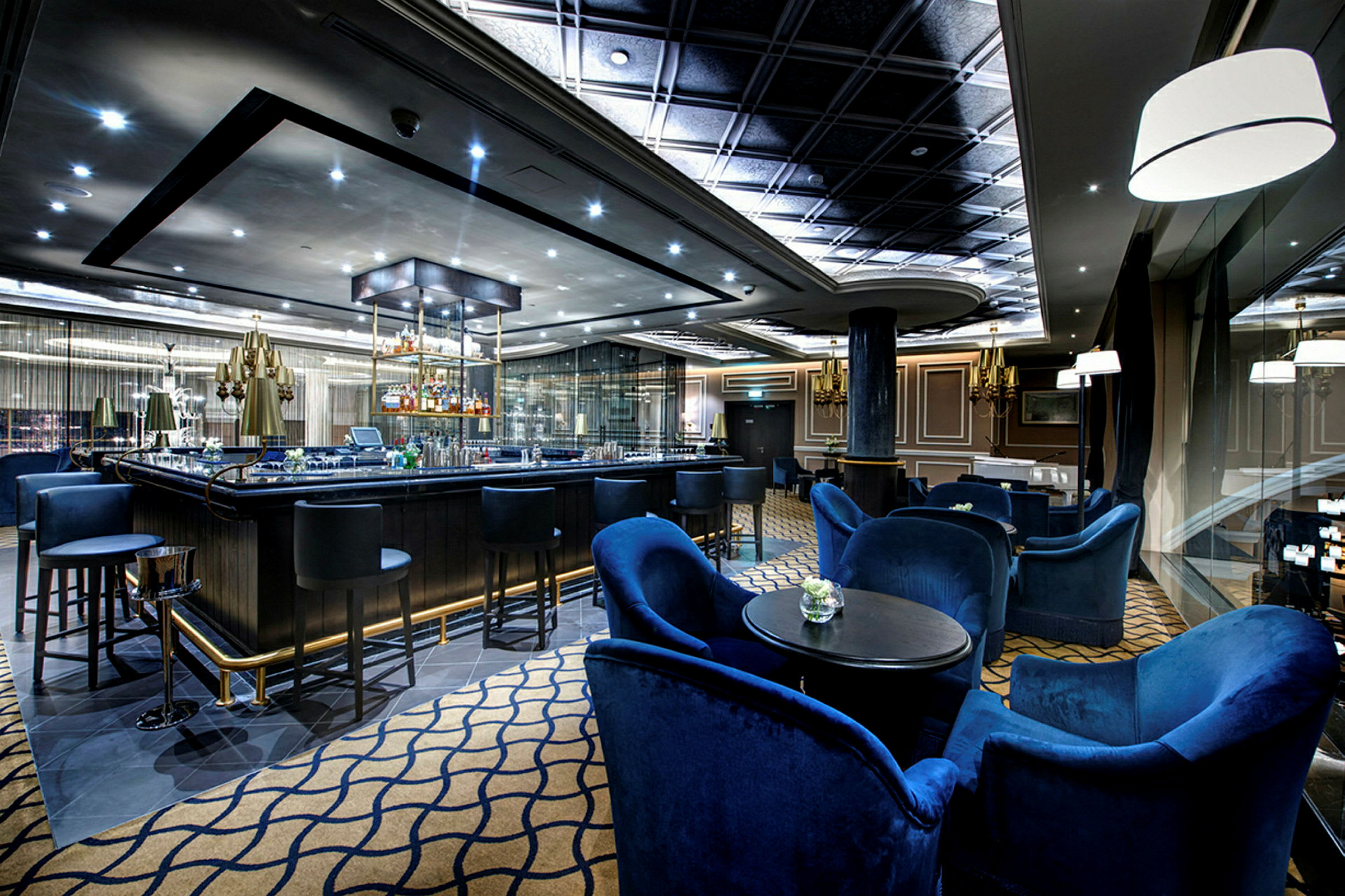 En elegant bar med blå stolar och bord, upplyst tak samt glasdetaljer. (AI-genererad text)