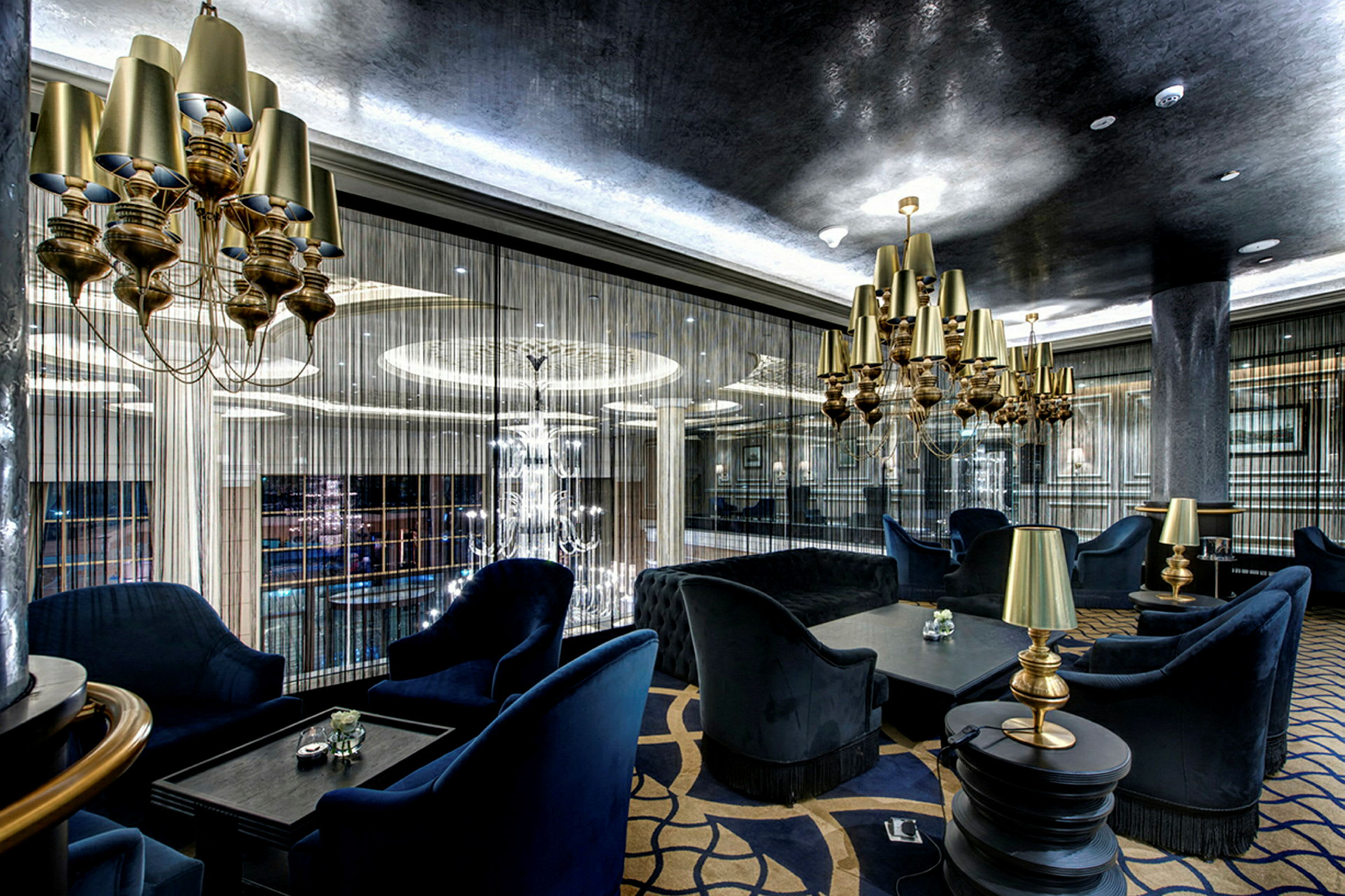 En elegant lounge med blå stoppade möbler, guldlampor och moderna hängande ljuskronor. (AI-genererad text)