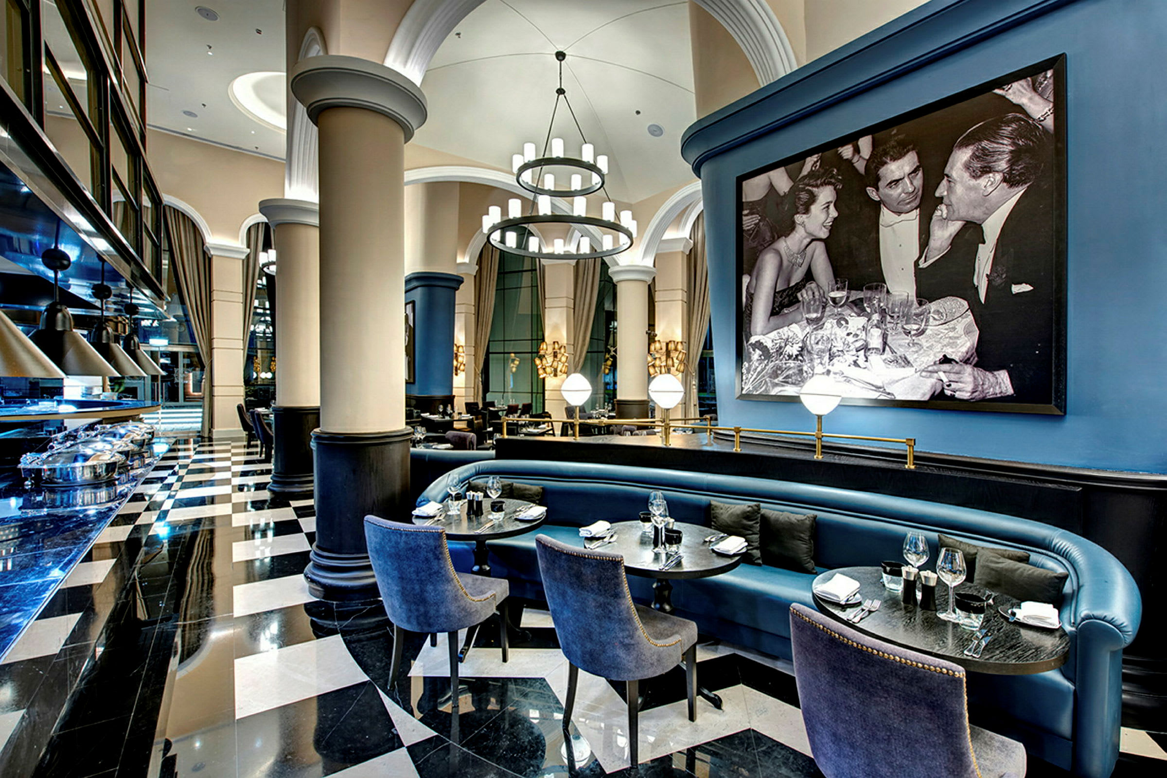 Interiör av en elegant restaurang med svartvitt golv, blå sittmöbler och en stor inramad svartvit bild. (AI-genererad text)