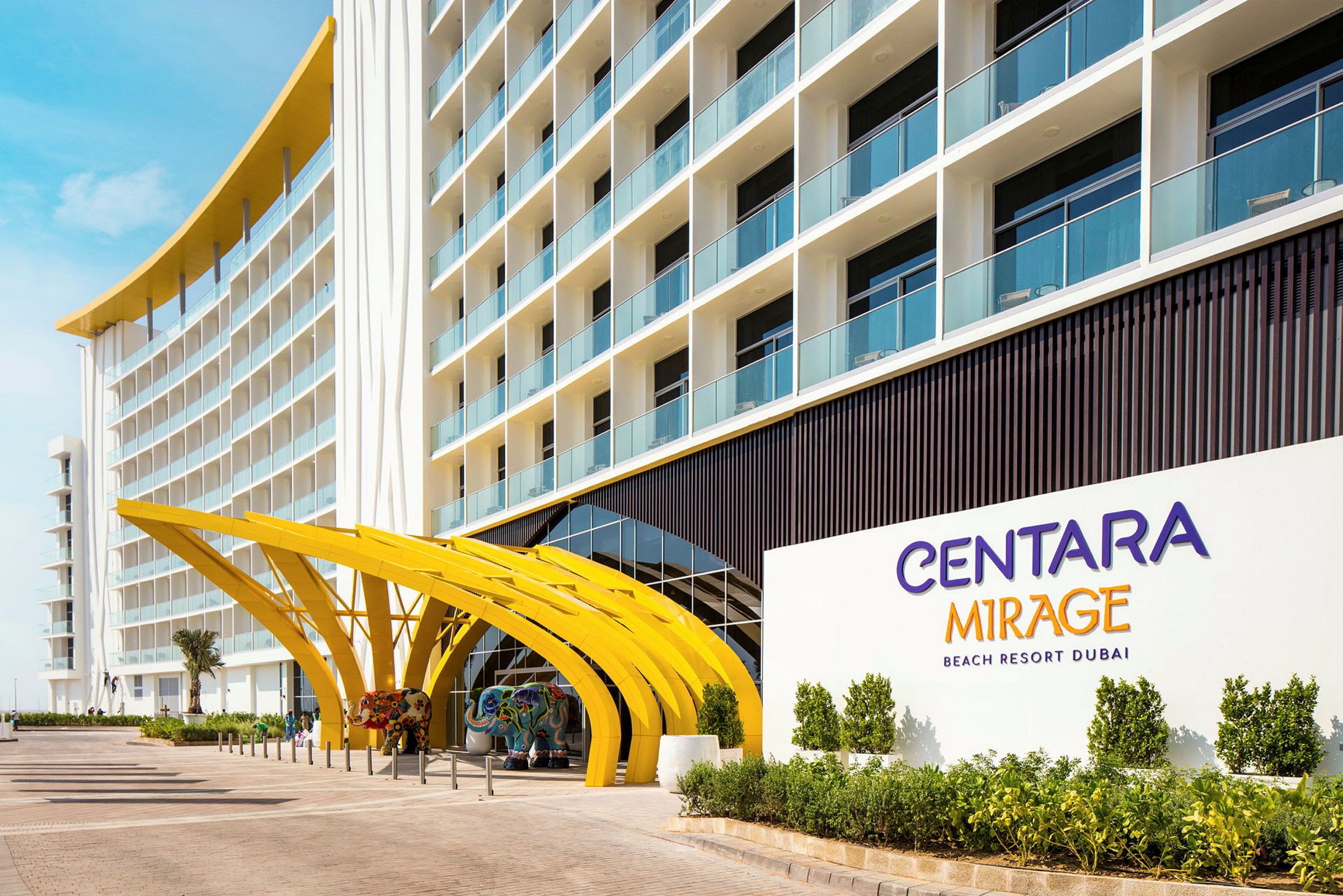 Entrén till ett hotell med bågformade gula strukturer och skylt som anger "Centara Mirage Beach Resort Dubai". (AI-genererad text)