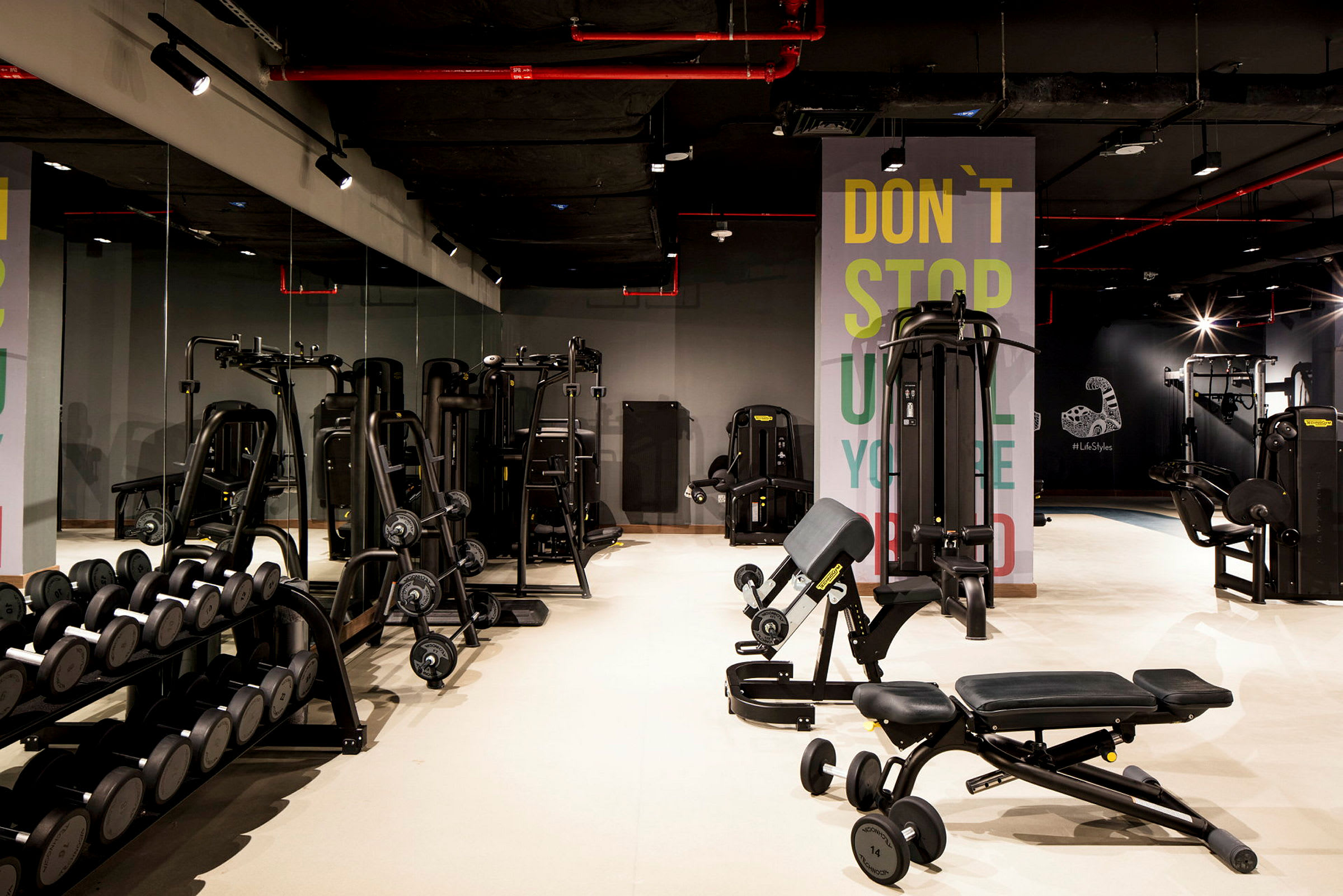 Ett gym med olika träningsmaskiner och hantlar på ett stativ, med en spegelvägg i bakgrunden. (AI-genererad text)