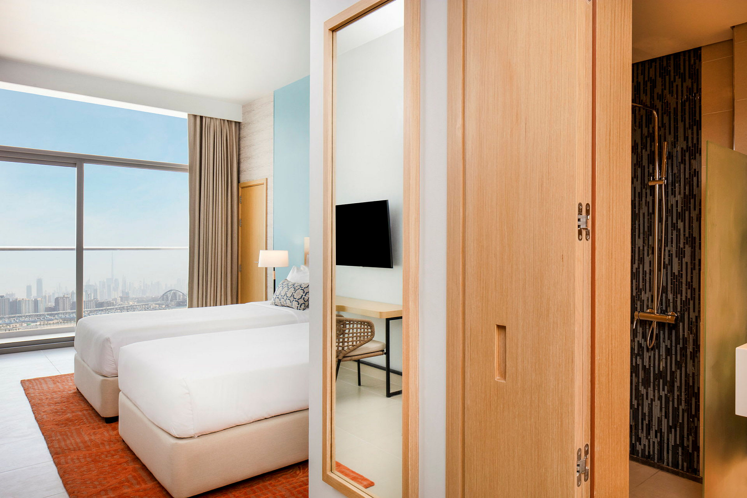 Ett modernt hotellrum med två enkelsängar som står nära ett stort fönster med utsikt över en stadshorisont. Ett badrum syns delvis till höger. (AI-genererad text)
