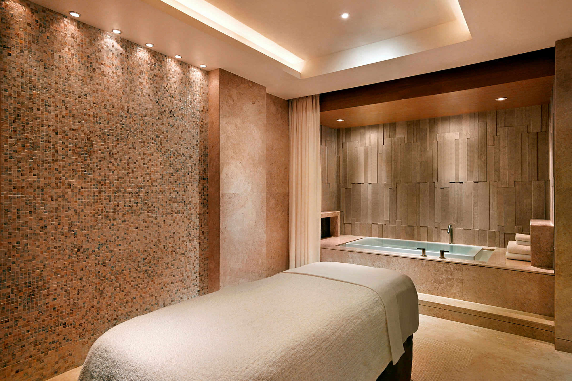 En spa-behandlingsrum med massagebänk och ett badkar i bakgrunden. (AI-genererad text)