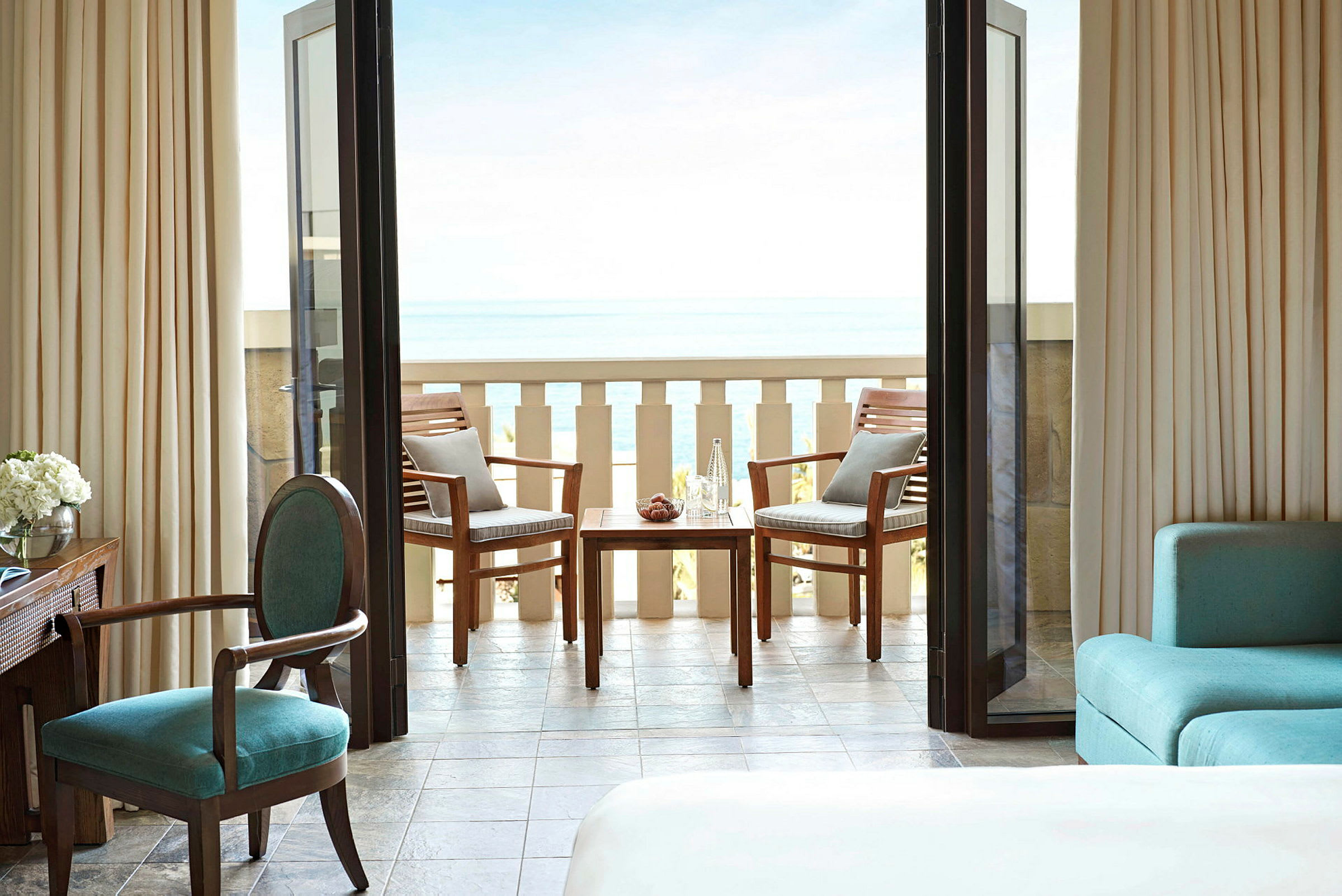 En hotellrumsbalkong med två trästolar och ett bord med utsikt över havet. (AI-genererad text)