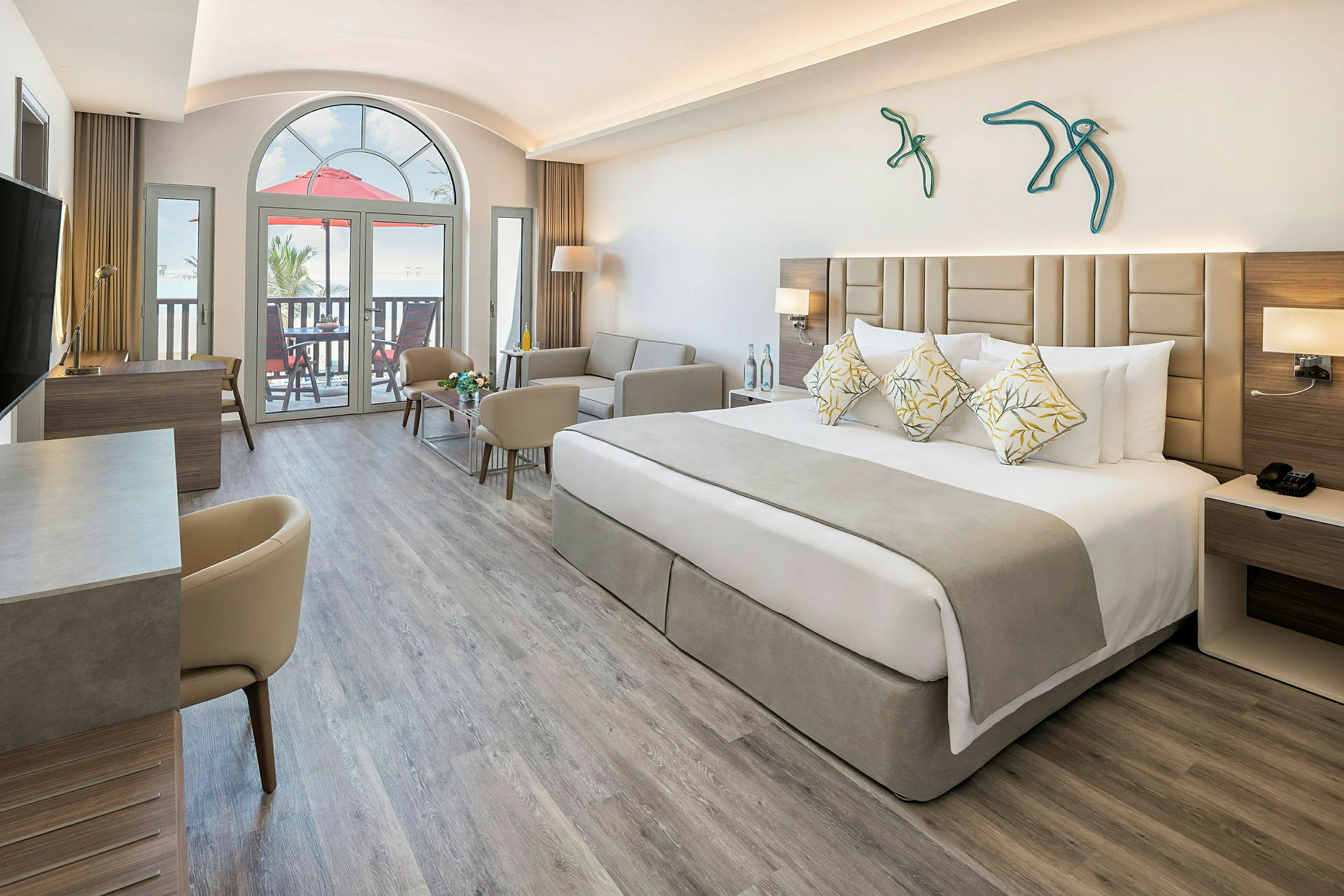 Ett modernt hotellrum med en bred säng, soffa och skrivbord. Stort fönster och balkong i bakgrunden. (AI-genererad text)