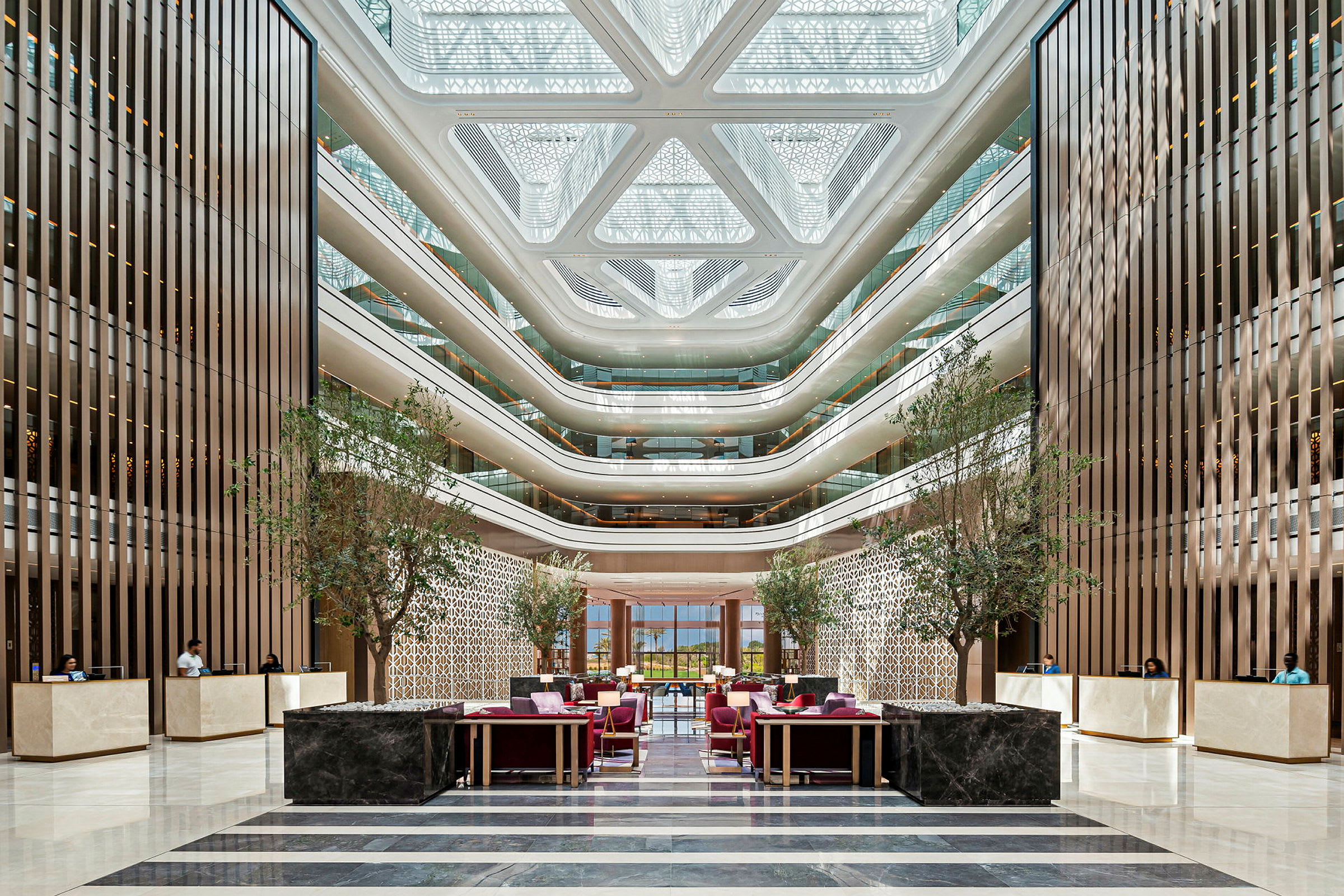 Bild av en modern hotellobby med eleganta sittgrupper, grönskande träd, receptionsdiskar och arkitektoniska detaljer. (AI-genererad text)