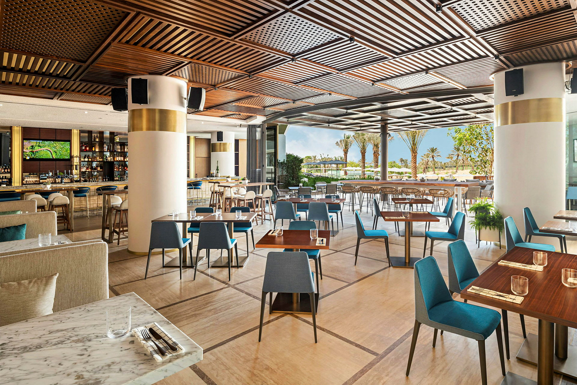 Restaurang med moderna bord och stolar samt öppning mot terrass med utsikt över palmer och grönska. (AI-genererad text)