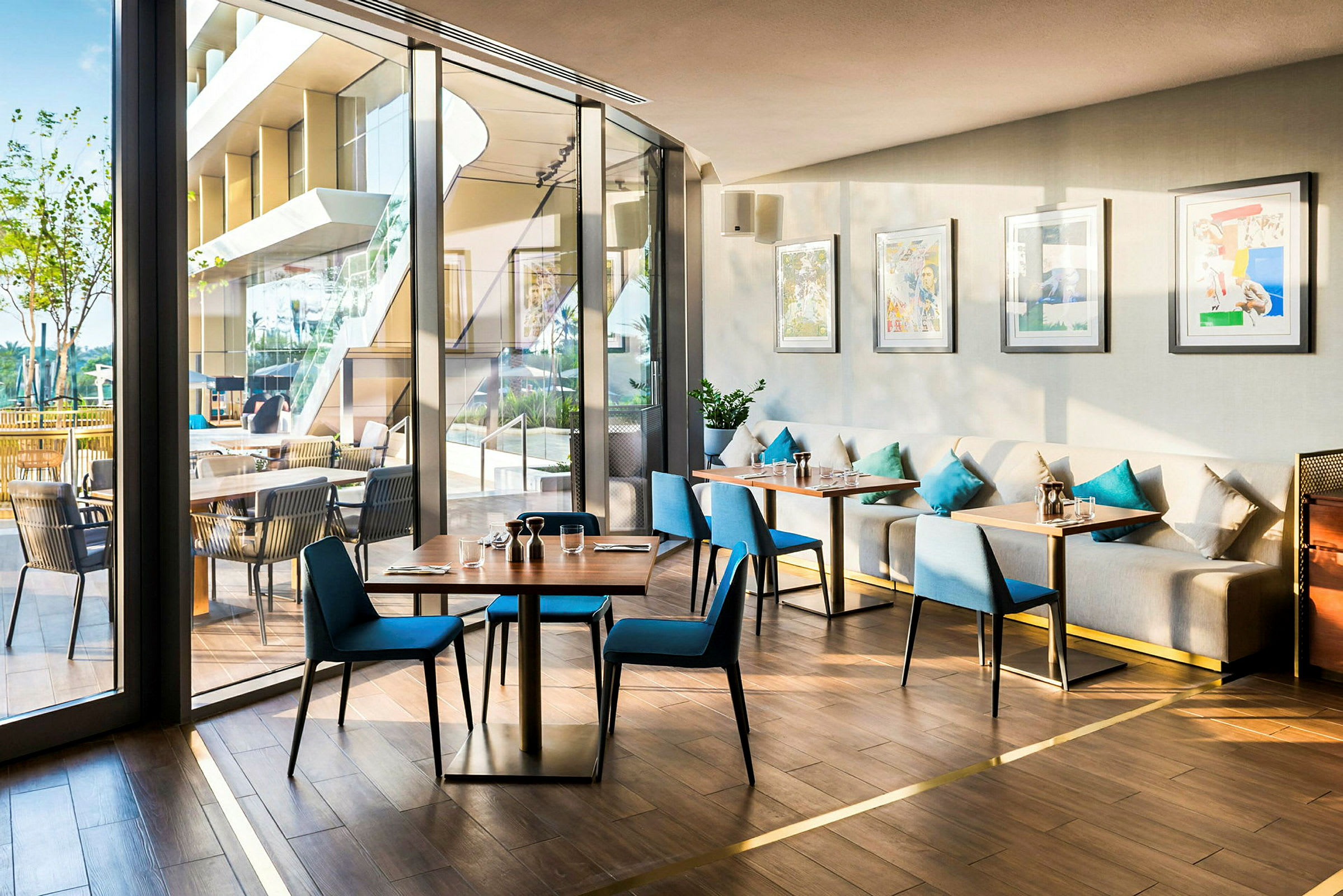 En ljus och modern restaurang med glasväggar, blå stolar och soffor med dekorativa kuddar. (AI-genererad text)