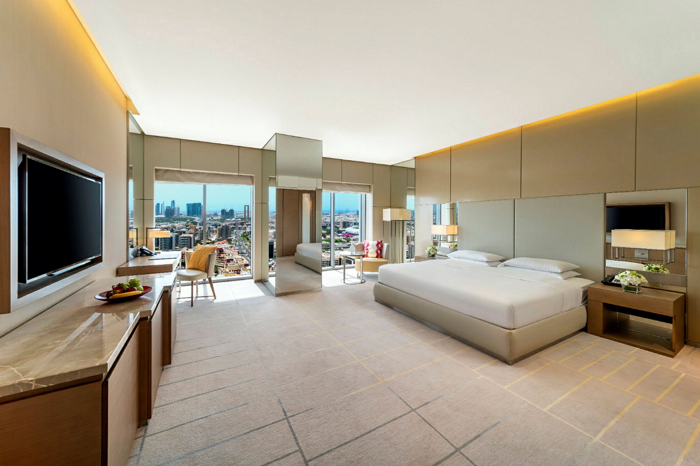 Modern hotellrum med stor säng, TV och utsikt över stadssilhuetten genom fönster. (AI-genererad text)