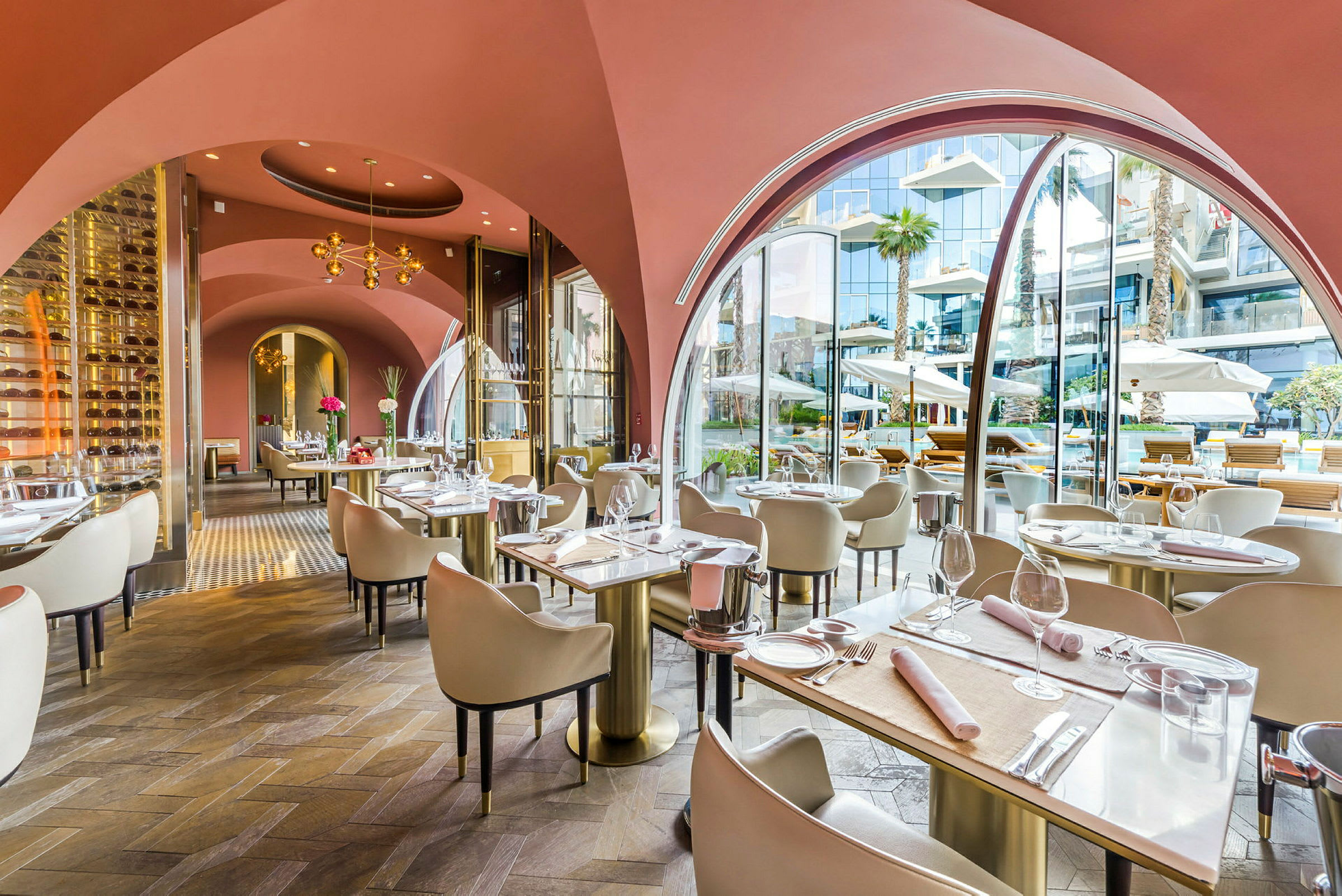 Interiören av en elegant restaurang med välvda rosa tak, matsalsmöbler och fönster mot en utomhusmiljö. (AI-genererad text)