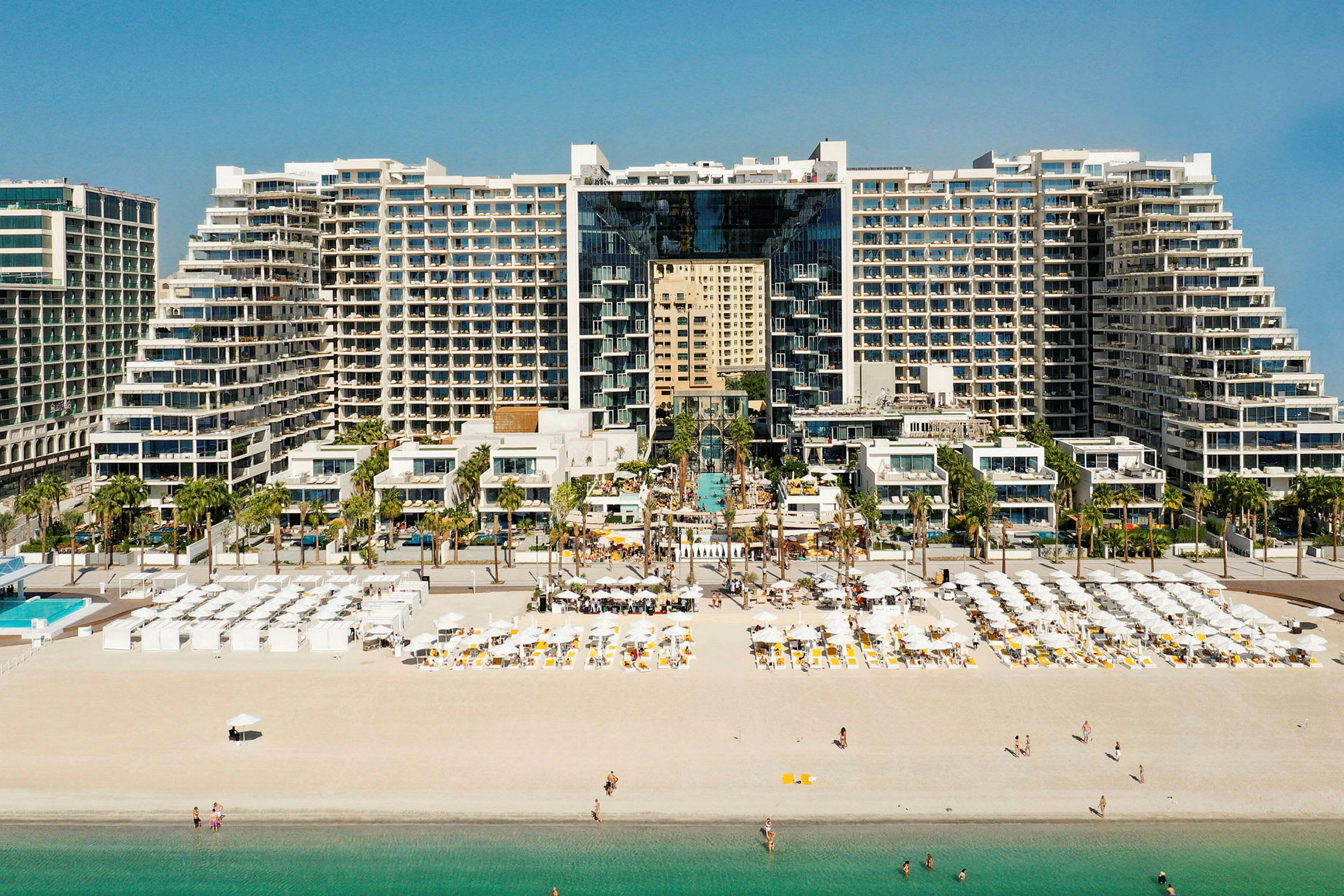En stor hotellbyggnad med modern arkitektur vid en sandstrand med solstolar och parasoller. (AI-genererad text)