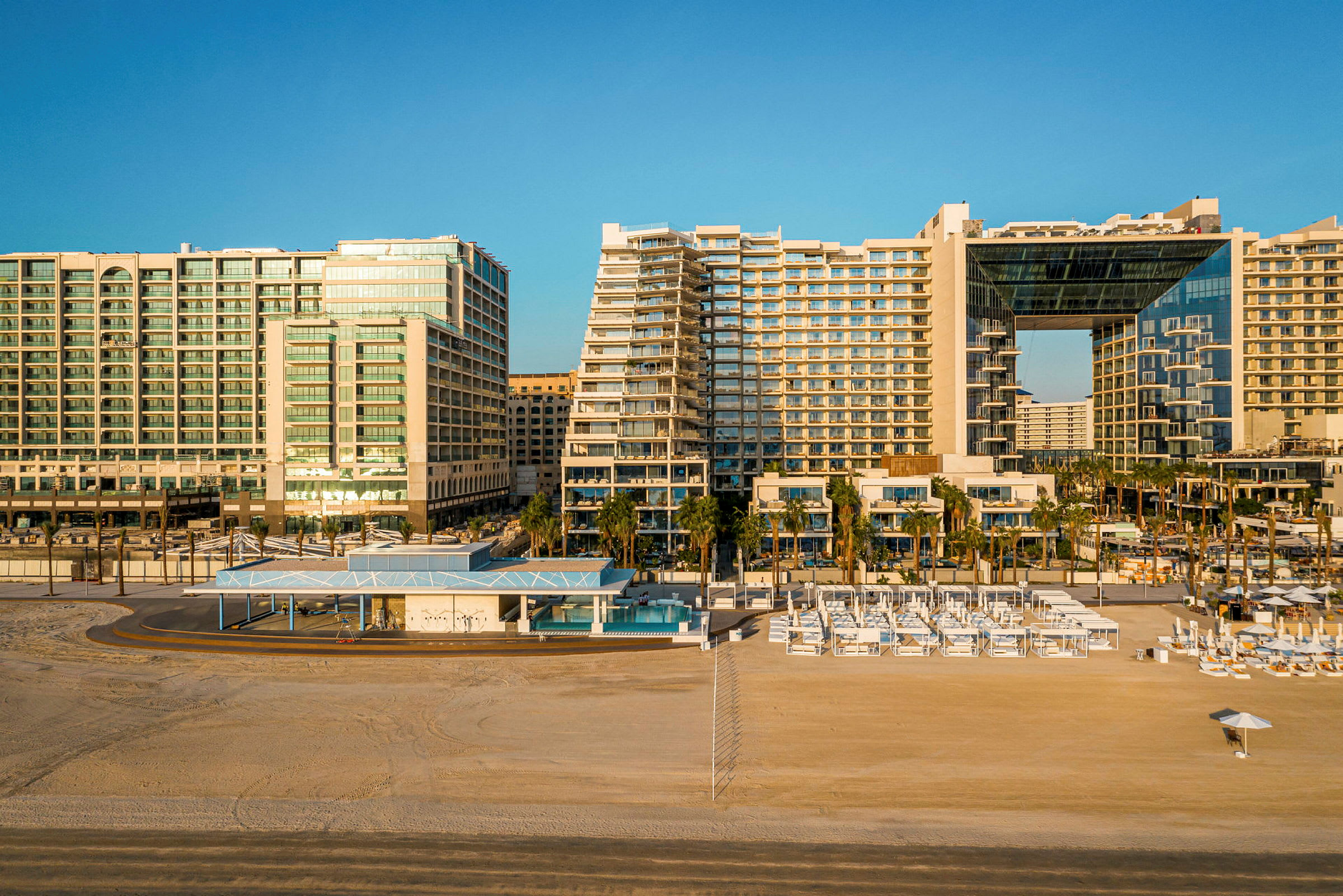 Bild av moderna hotellbyggnader vid en strand med solstolar och parasoller. (AI-genererad text)