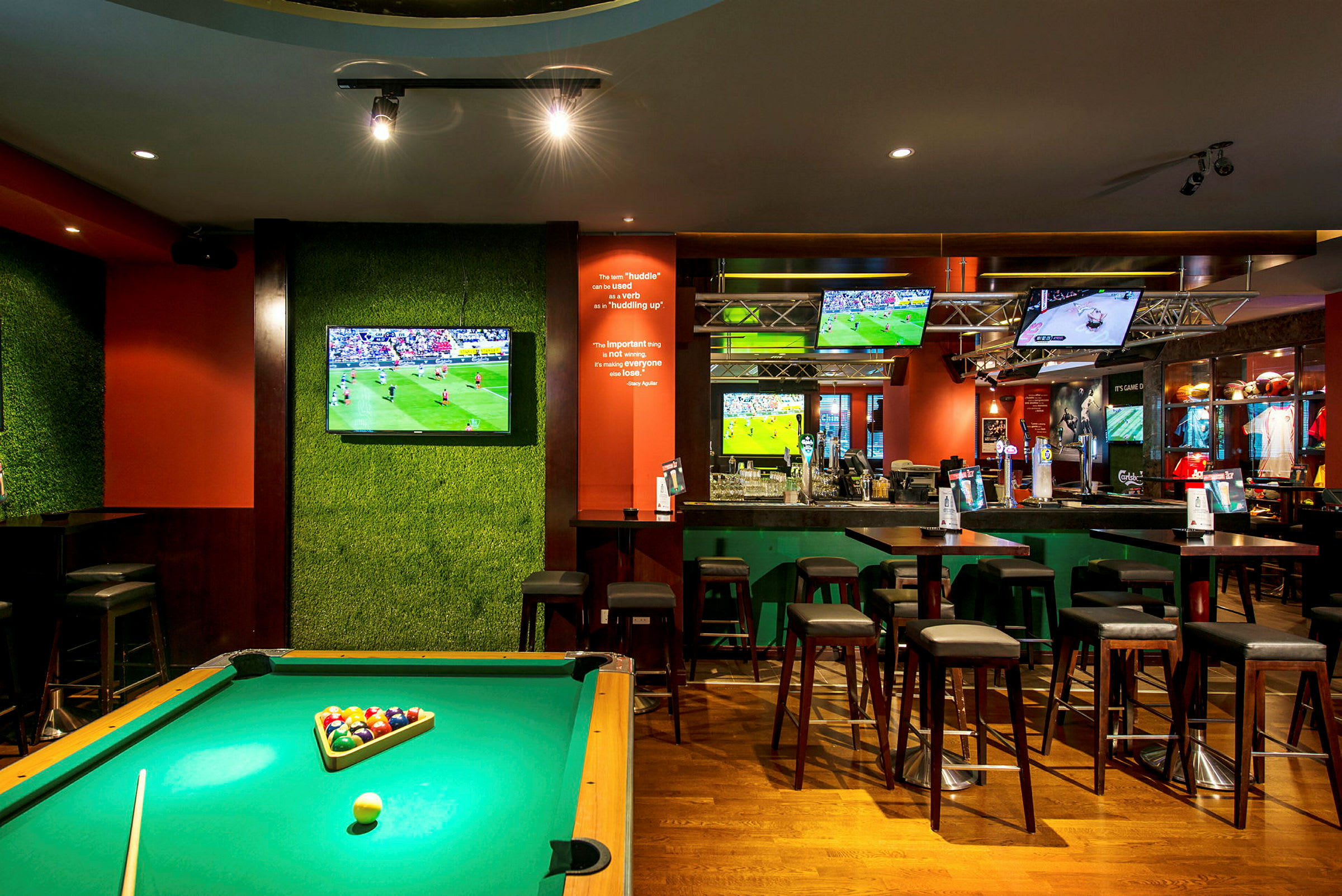 Ett biljardbord i en bar med flera TV-skärmar som visar sport. (AI-genererad text)