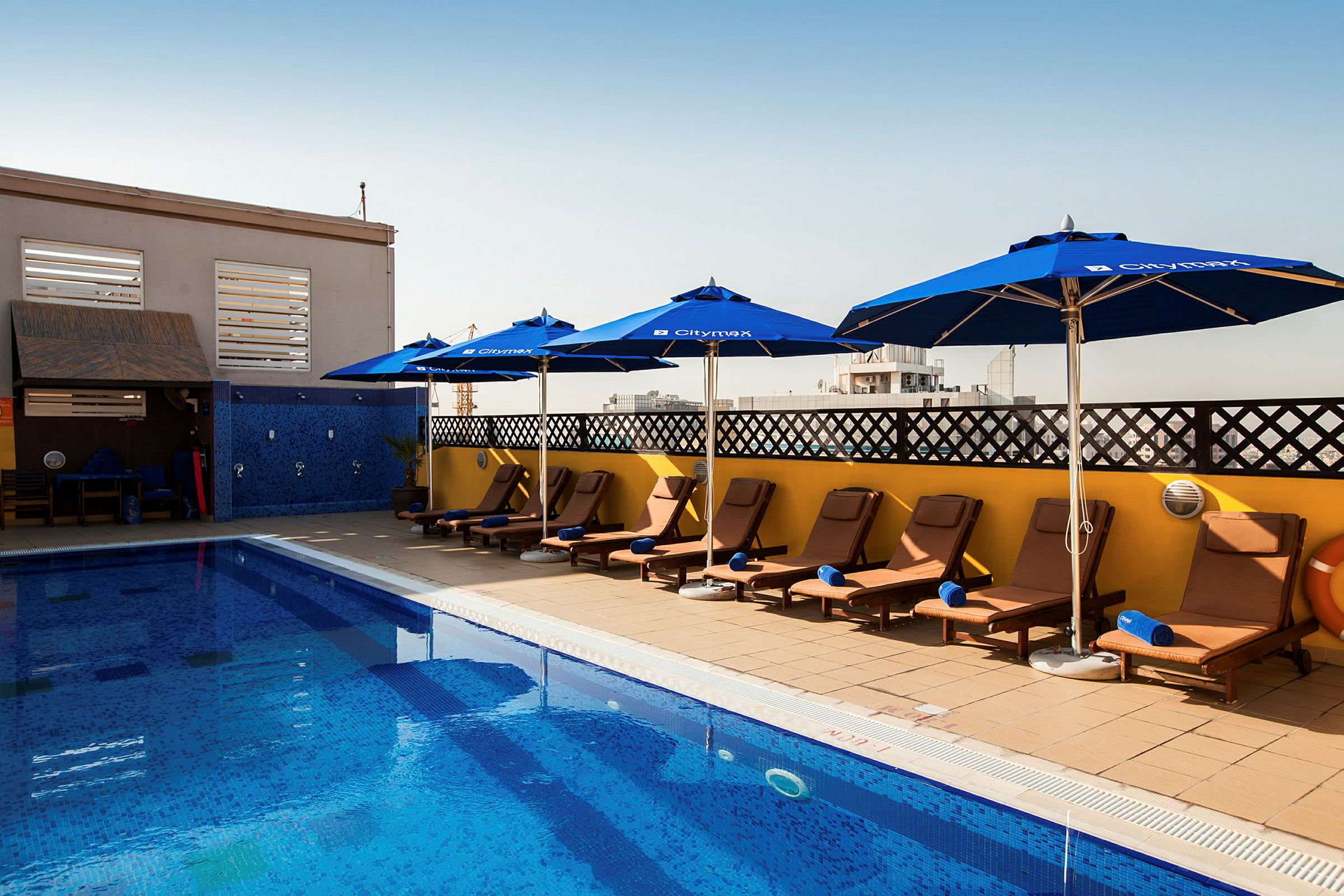 En pool med solstolar och parasoller vid sidan under en klar himmel. (AI-genererad text)
