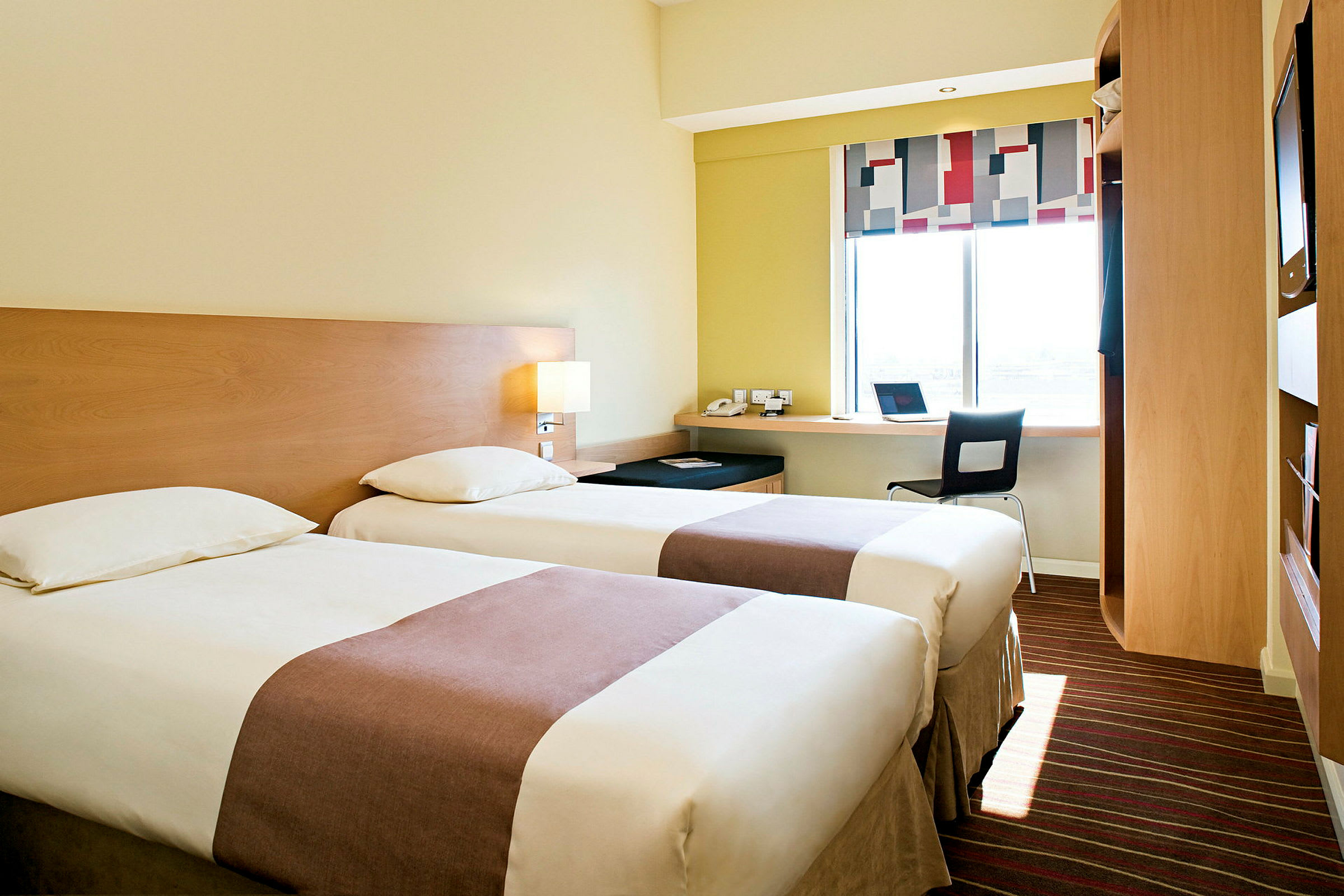 Ett hotellrum med två enkelsängar, en arbetsstation vid ett fönster och moderna möbler. (AI-genererad text)
