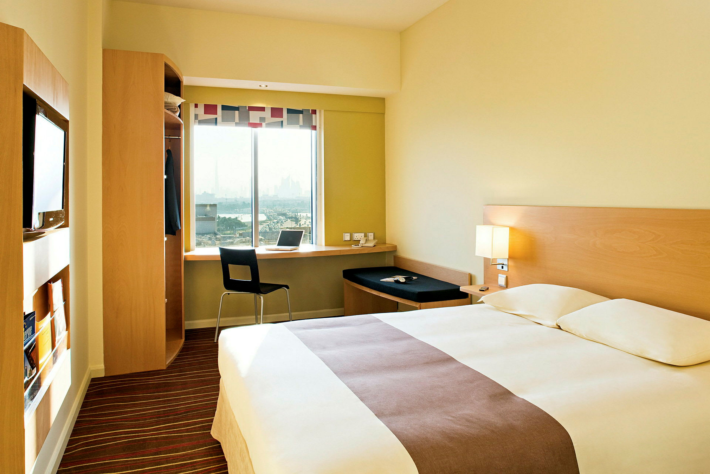 Ett hotellrum med en dubbelsäng, ett skrivbord vid ett fönster och en garderob. (AI-genererad text)