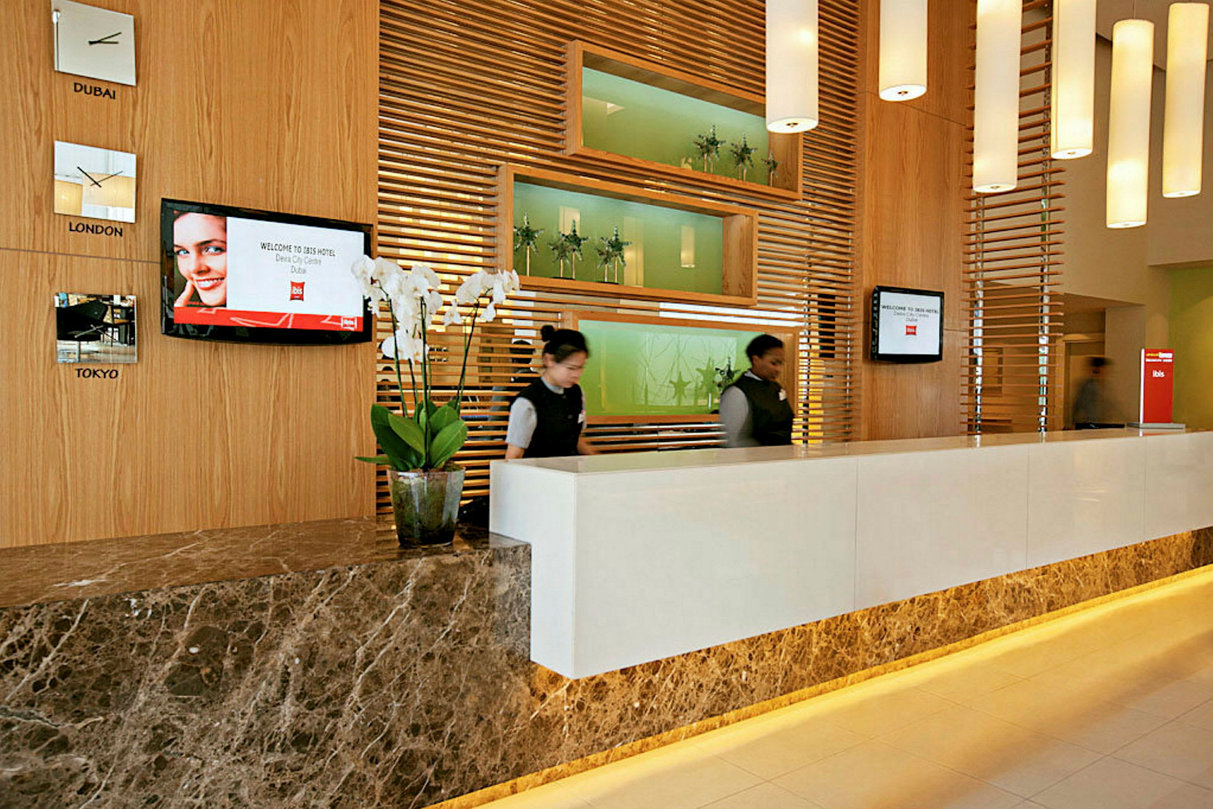 En receptionsdisk i ett hotell med träpaneler, dekorativa väggreliefer och vita vägglampor. (AI-genererad text)