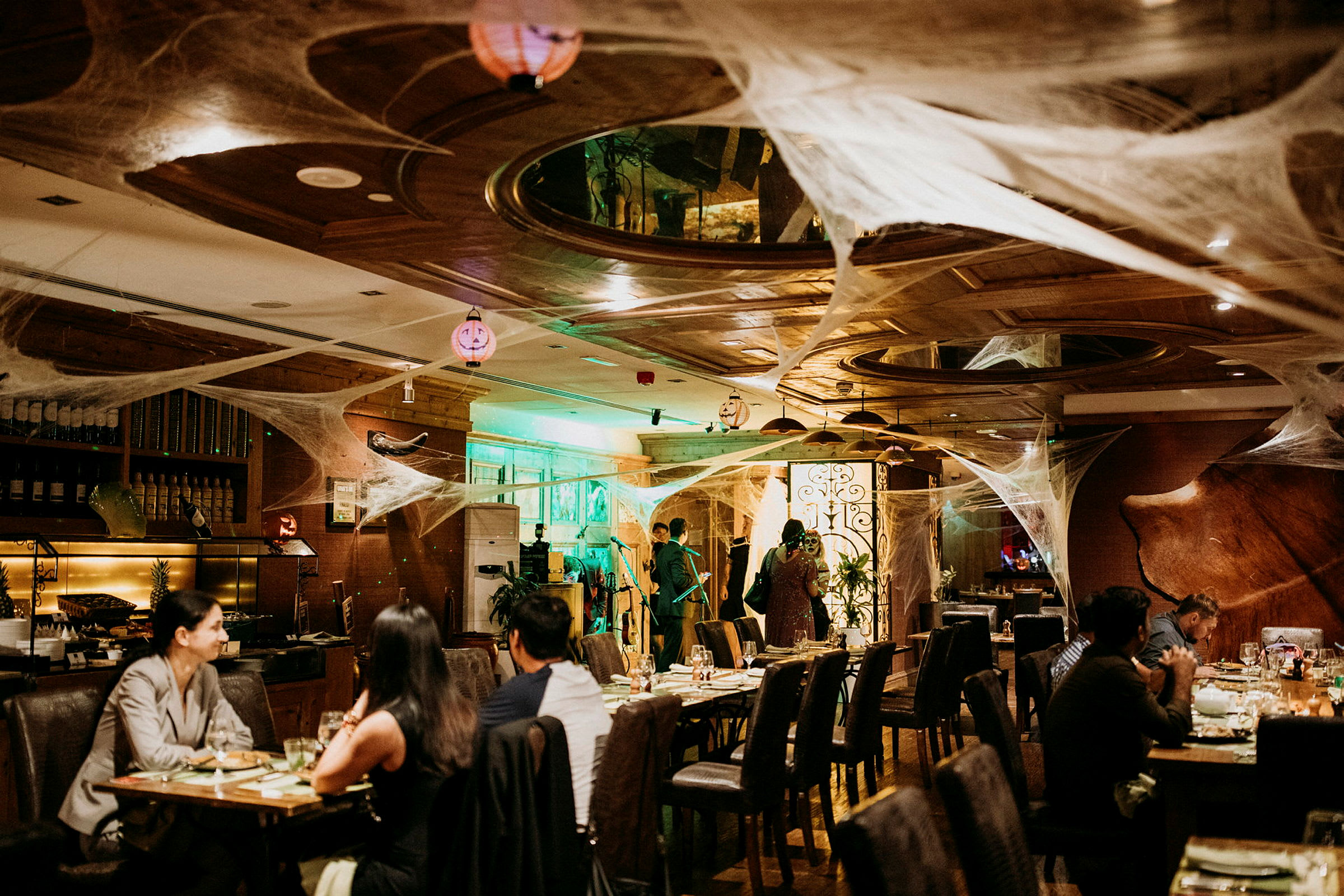 En restaurang interiör dekorerad med spindelvävsliknande prydnader och belysning, med gäster vid bord och personal i bakgrunden. (AI-genererad text)