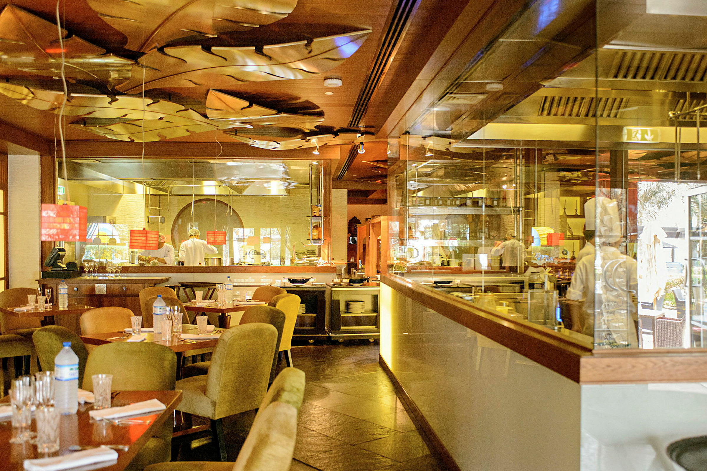 Ett interiörfoto av en restaurang med bord och stolar, ett öppet kök i bakgrunden och en dekorativ inredning med reflekterande ytor. (AI-genererad text)
