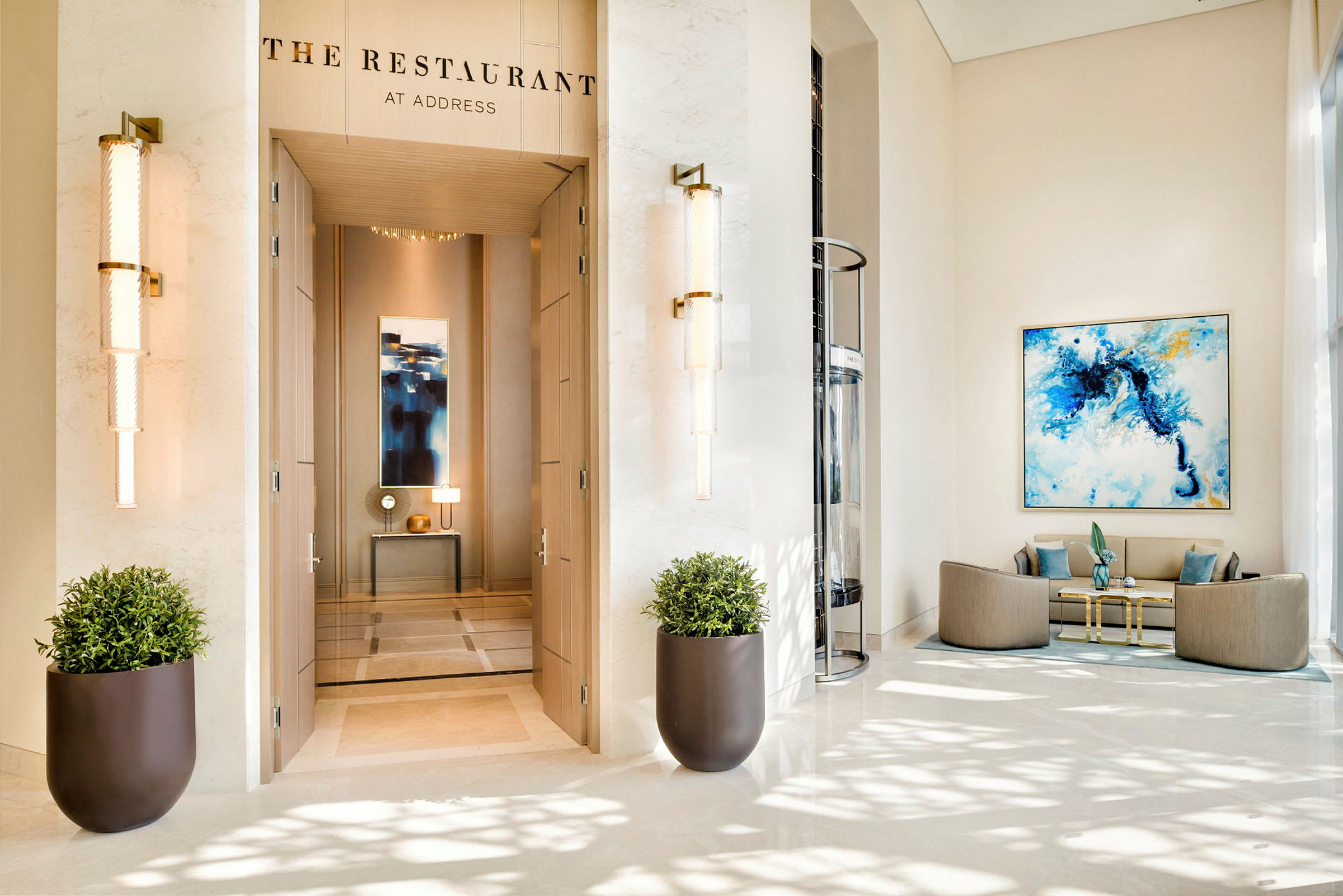 En elegant hotellobby med entrén till "The Restaurant" synlig, två stora blomkrukor, och en sittgrupp till höger. (AI-genererad text)