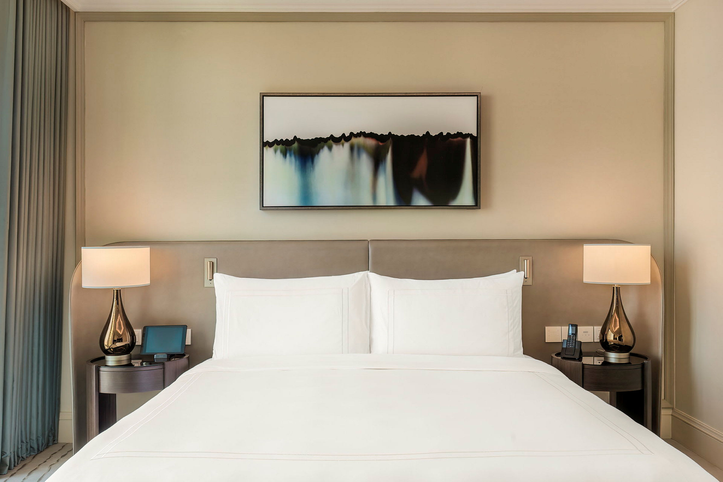 Ett välbäddat hotellsäng med två nattduksbord och lampor på vardera sida, samt en tavla ovanför sängens huvudgavel. (AI-genererad text)