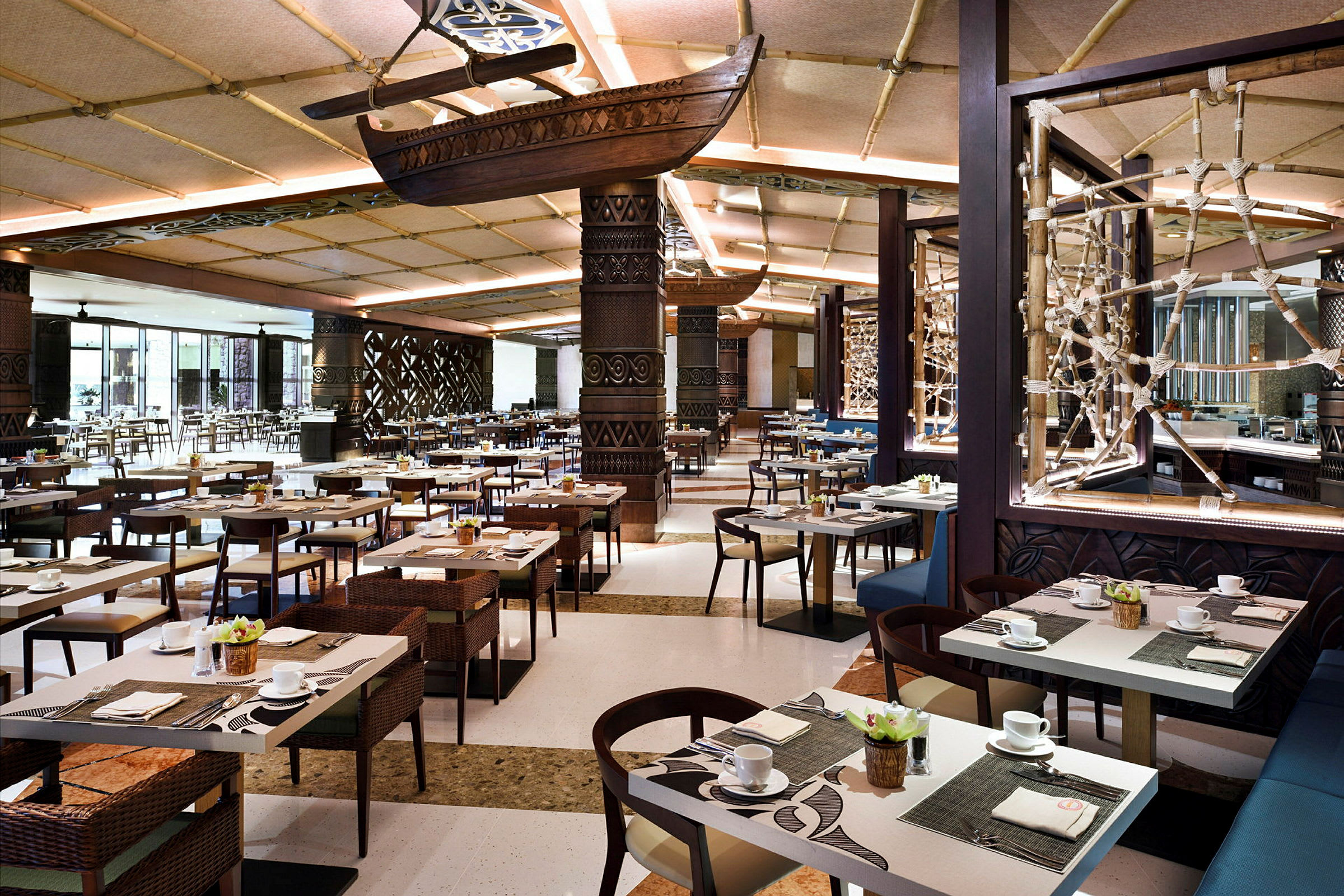 Inredning i en rymlig restaurang med bord dukade för måltider, dekorerade tak och väggar. Ett skepp hänger från taket som en del av dekoren. (AI-genererad text)