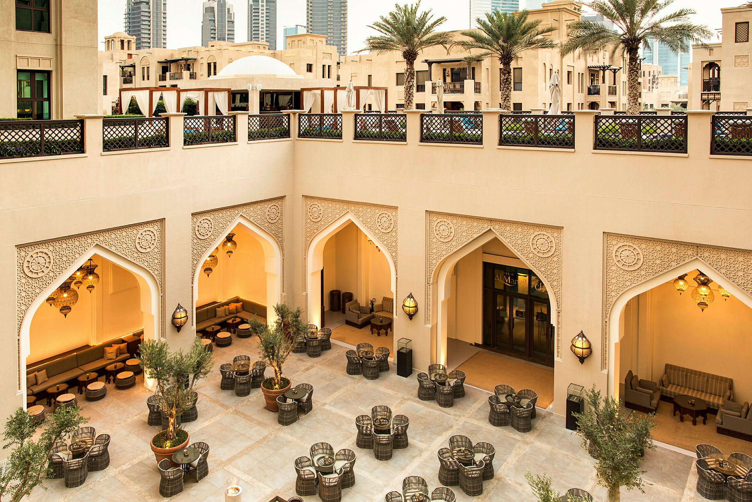 Välutformad innergård med sittgrupper, prydnader av orientaliska valv och belysning, samt omgiven av modern och traditionell arkitektur. (AI-genererad text)